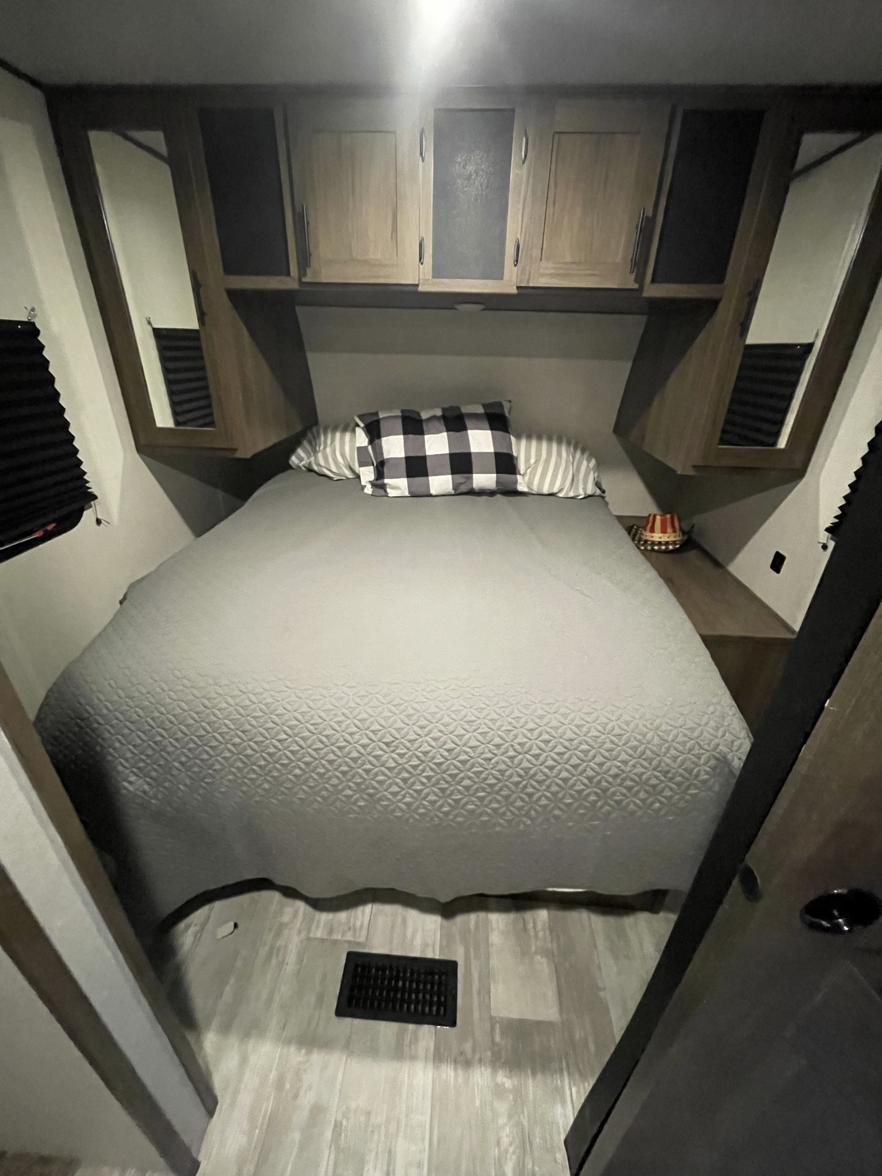 A cozy and well-equipped RV rental bedroom featuring a bed with patterned gray bedding, overhead storage, and side tables.. Forrest River Prime Time Avenger 2021