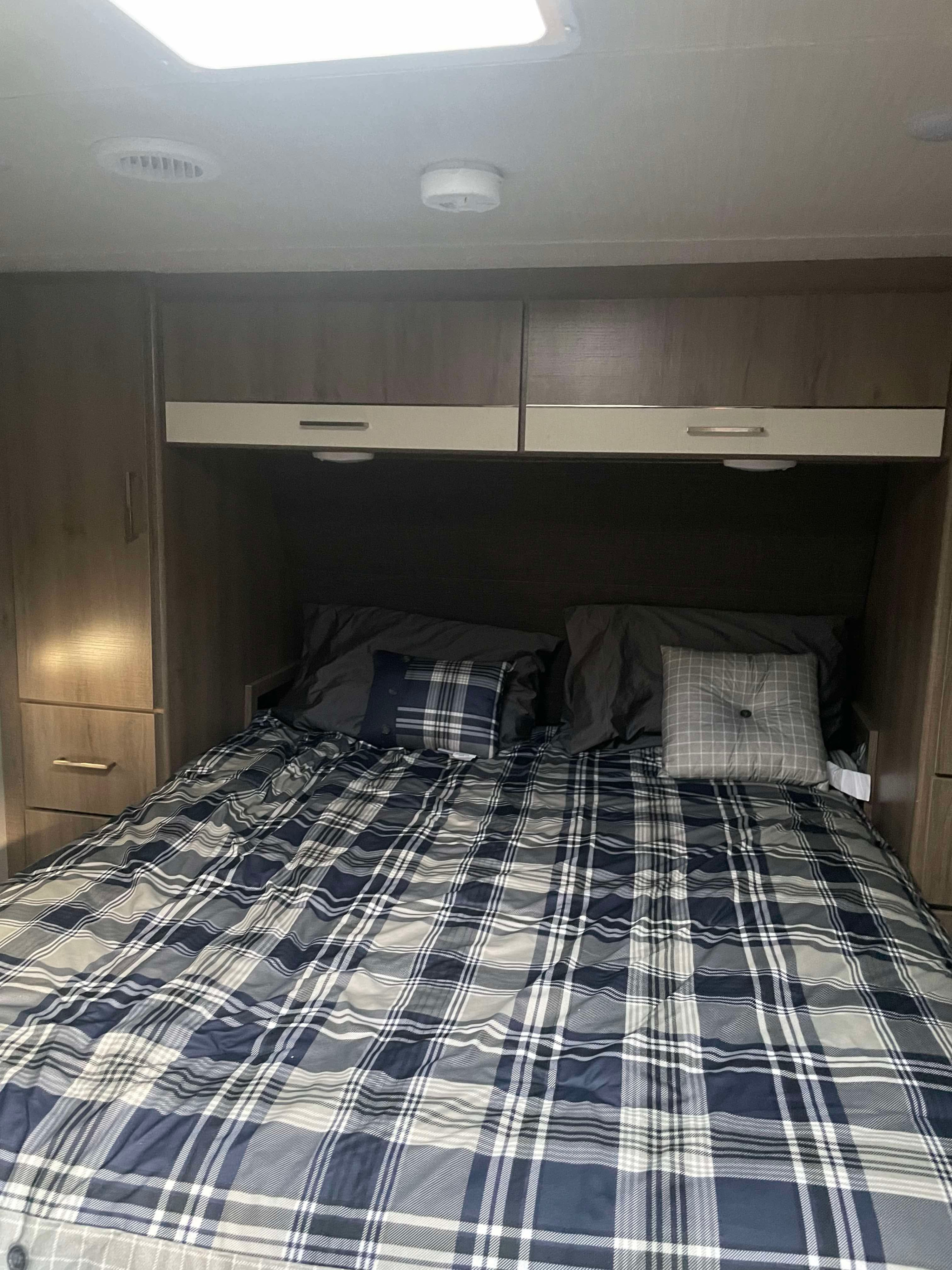 Cozy RV rental bedroom with plaid bedding, overhead cabinets, and built-in storage, perfect for travel.. Grand Design Imagine XLS 2022