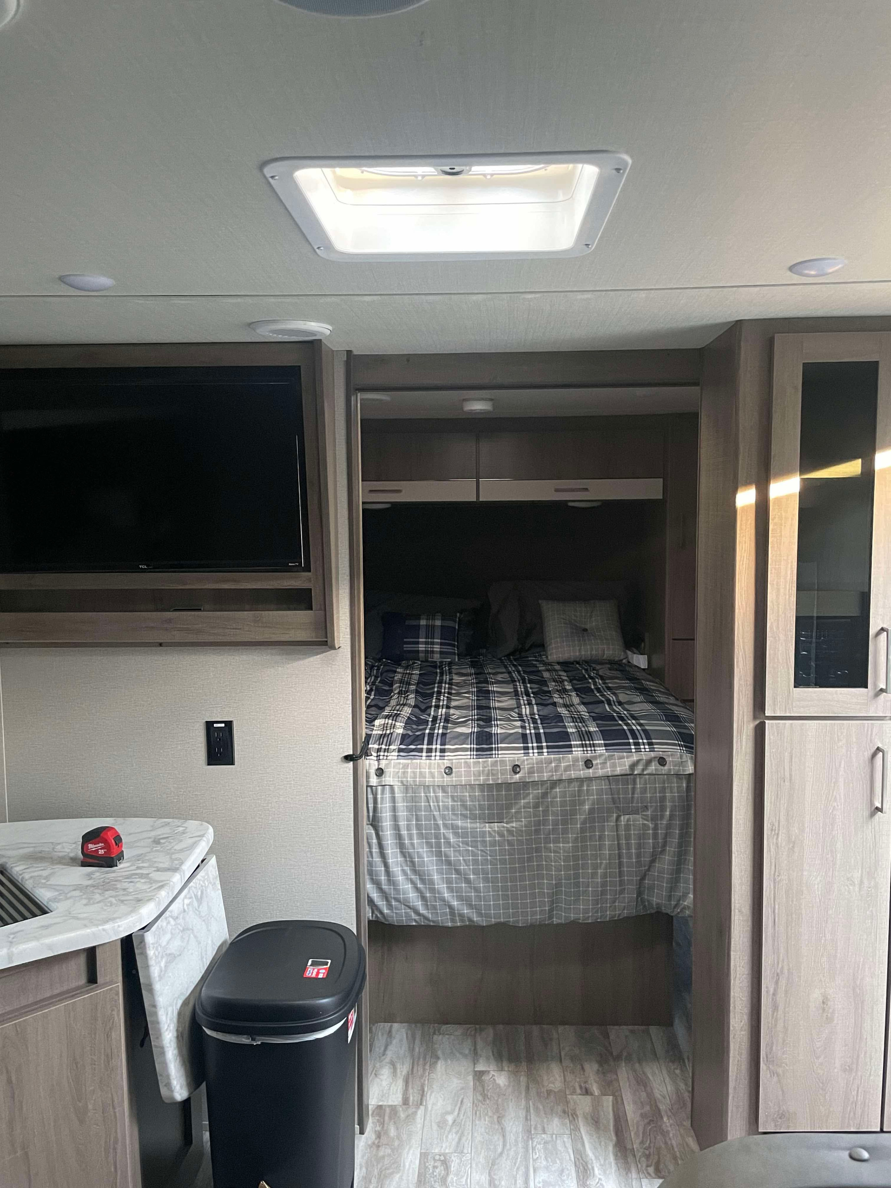 Cozy RV rental interior: bedroom with plaid bedding, compact kitchen, TV, and skylight. Perfect for travel.. Grand Design Imagine XLS 2022