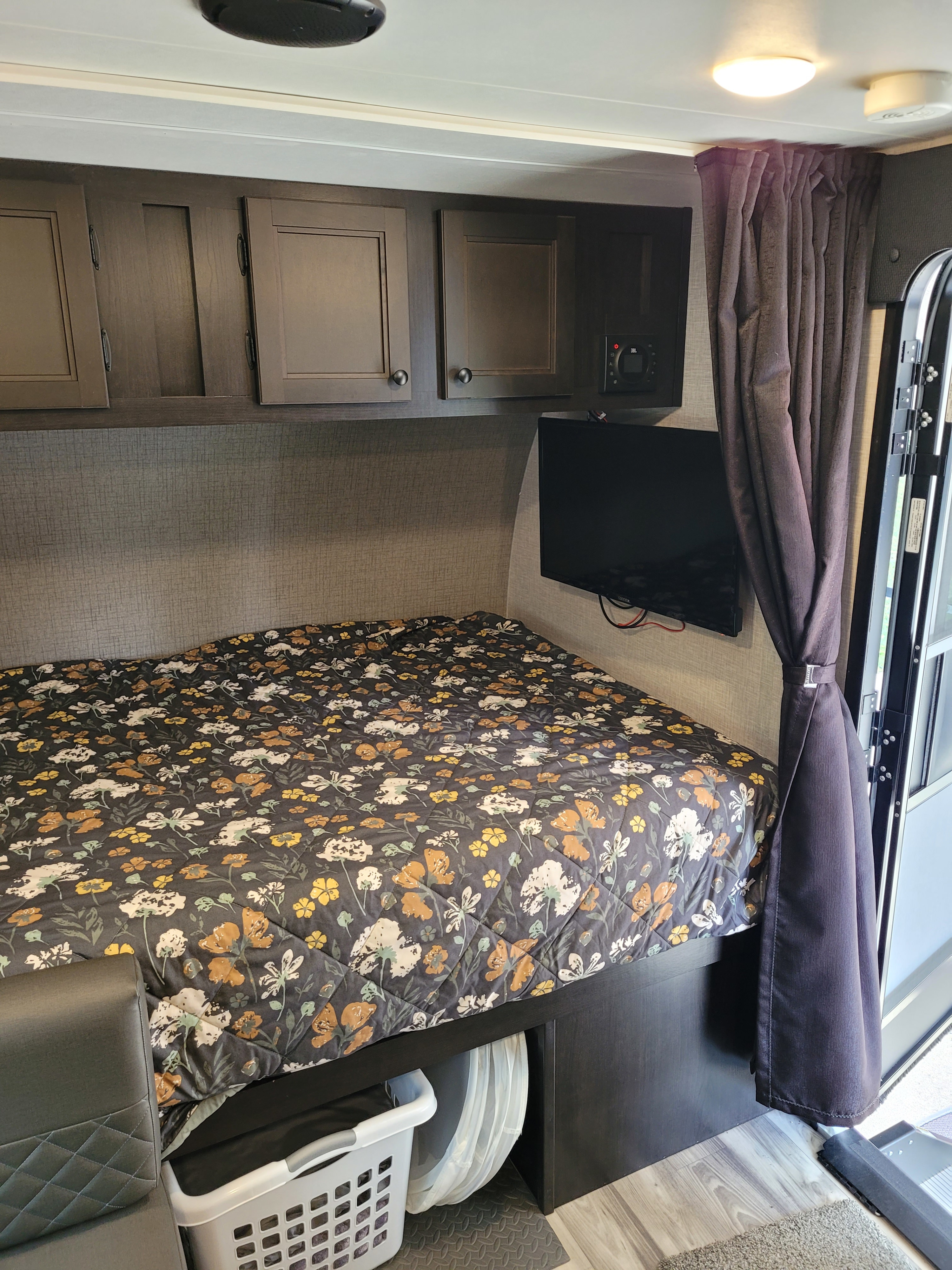 RV rental interior: cozy bedroom with floral bed, overhead cabinets, mounted TV, and under-bed storage. Compact comfort.. Starcraft Super Lite Maxx 2023