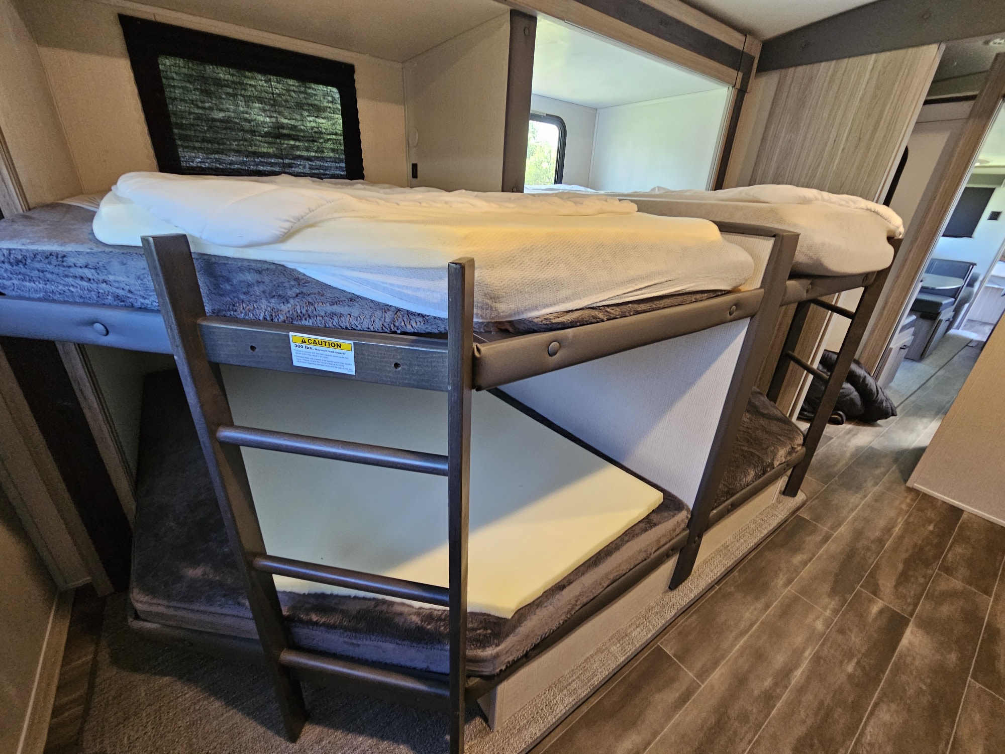 Inside an RV rental, comfortable bunk beds are shown, with mattresses, foam toppers, and a window.. Keystone RV Passport GT 2022