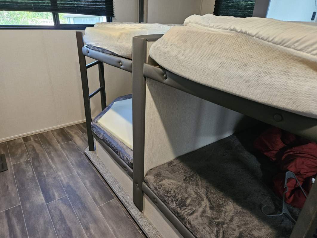 RV rental interior features spacious bunk beds. Mattresses are visible, with cozy bedding on lower bunks. Perfect for family trips.. Keystone RV Passport GT 2022