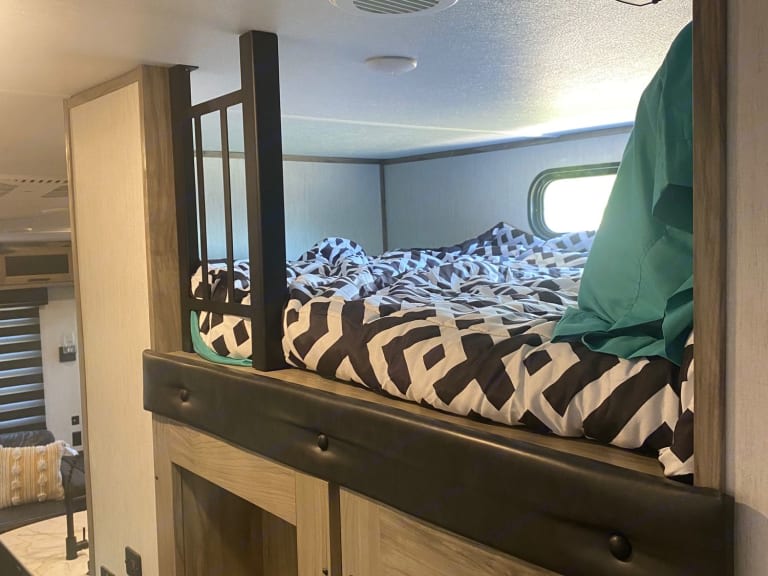 Cozy RV rental interior: a bunk bed with a modern black & white patterned comforter and safety rail, ideal for travel.. Forest River Cherokee Arctic Wolf 2021