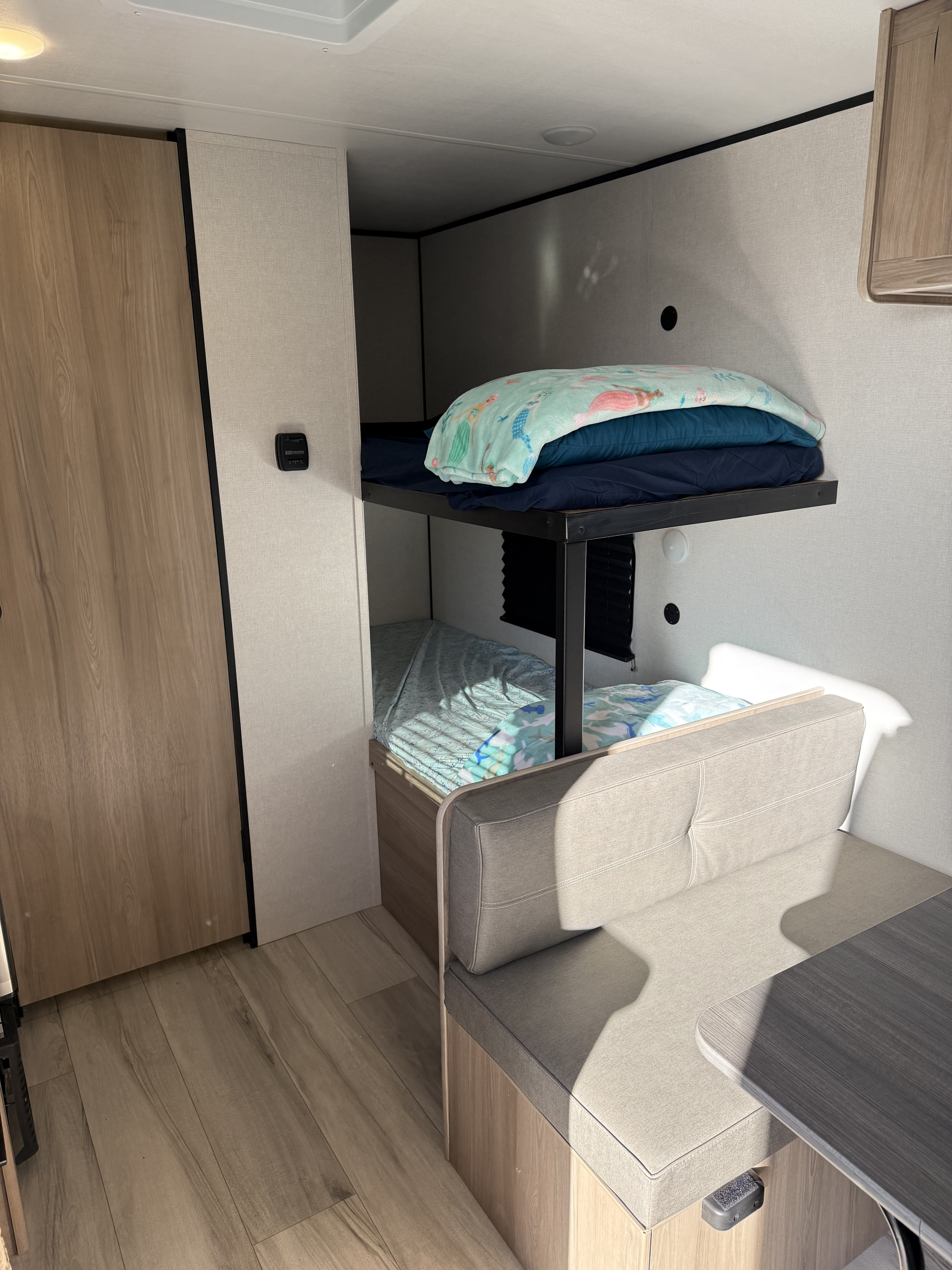 This RV rental features cozy bunk beds with light blue bedding, a tan dinette, and wood-look flooring in a compact space.. Keystone Coleman 17B 2025