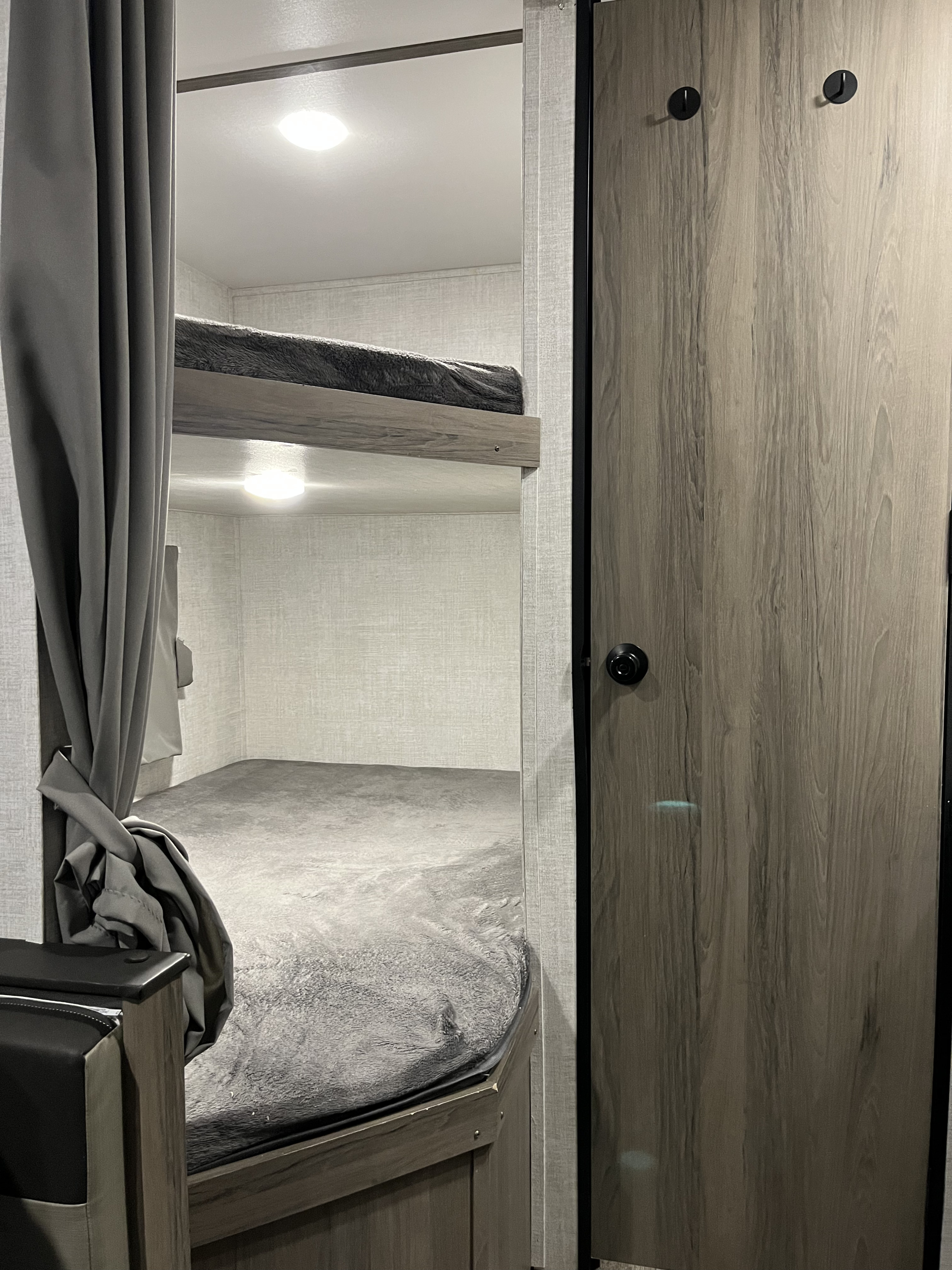 Inside an RV rental: a view of neatly made bunk beds with grey bedding, ambient lighting, and a practical interior.. Gulf Stream Conquest 2022