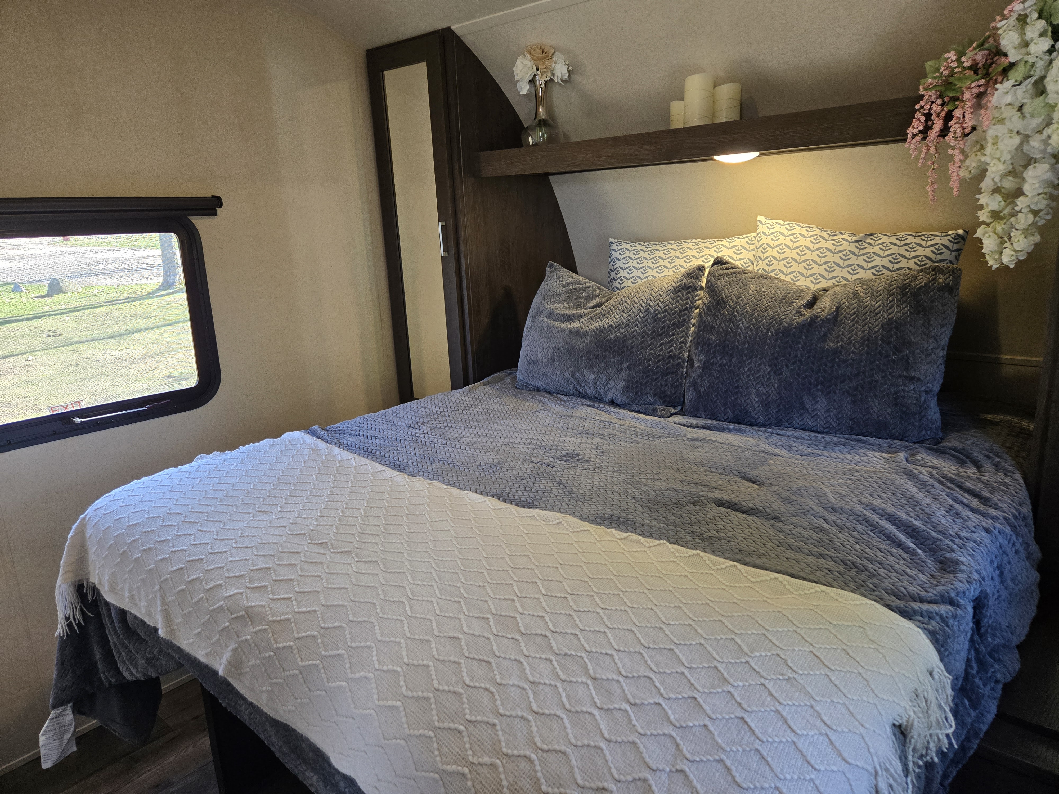 Inviting RV rental bedroom: cozy bed with patterned pillows, shelf decor, and window showing park scenery.. Forest River Salem 2018