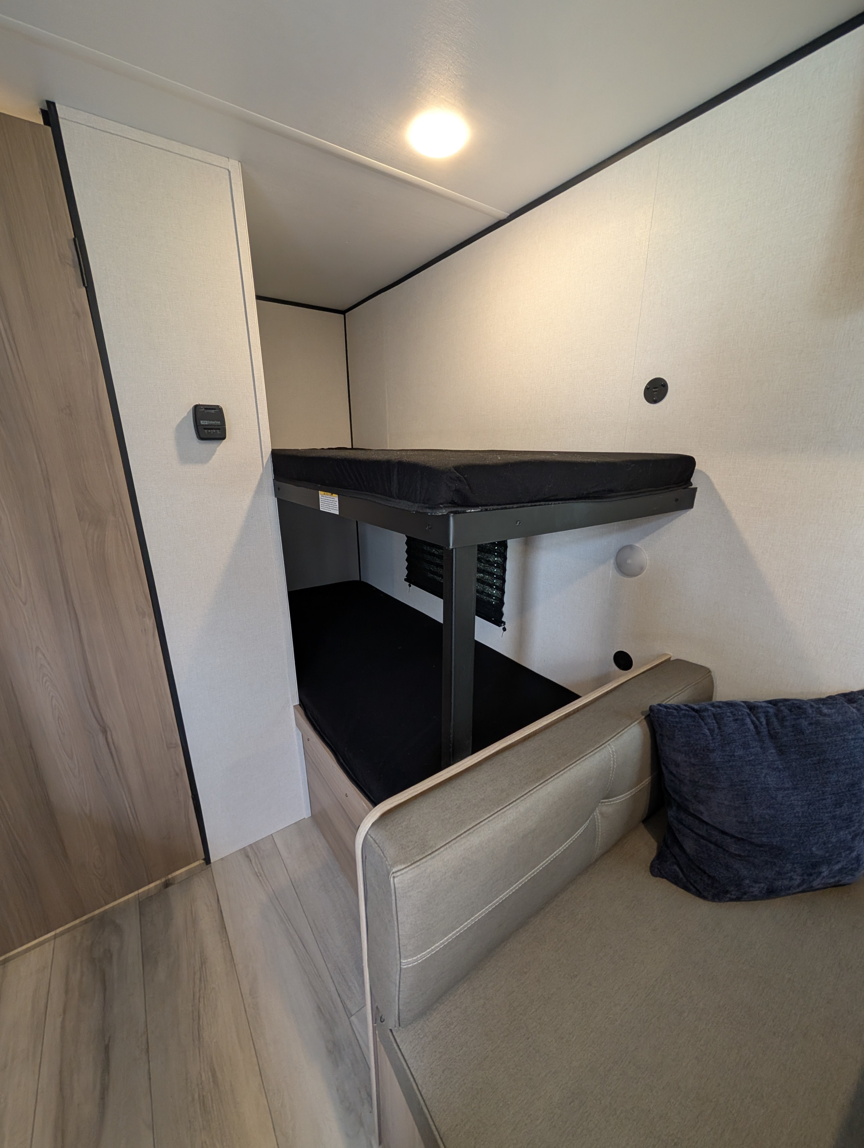 An RV rental's compact interior, showcasing a sleeping area with bunk beds and a seating area with a sofa.. Keystone Coleman 2025