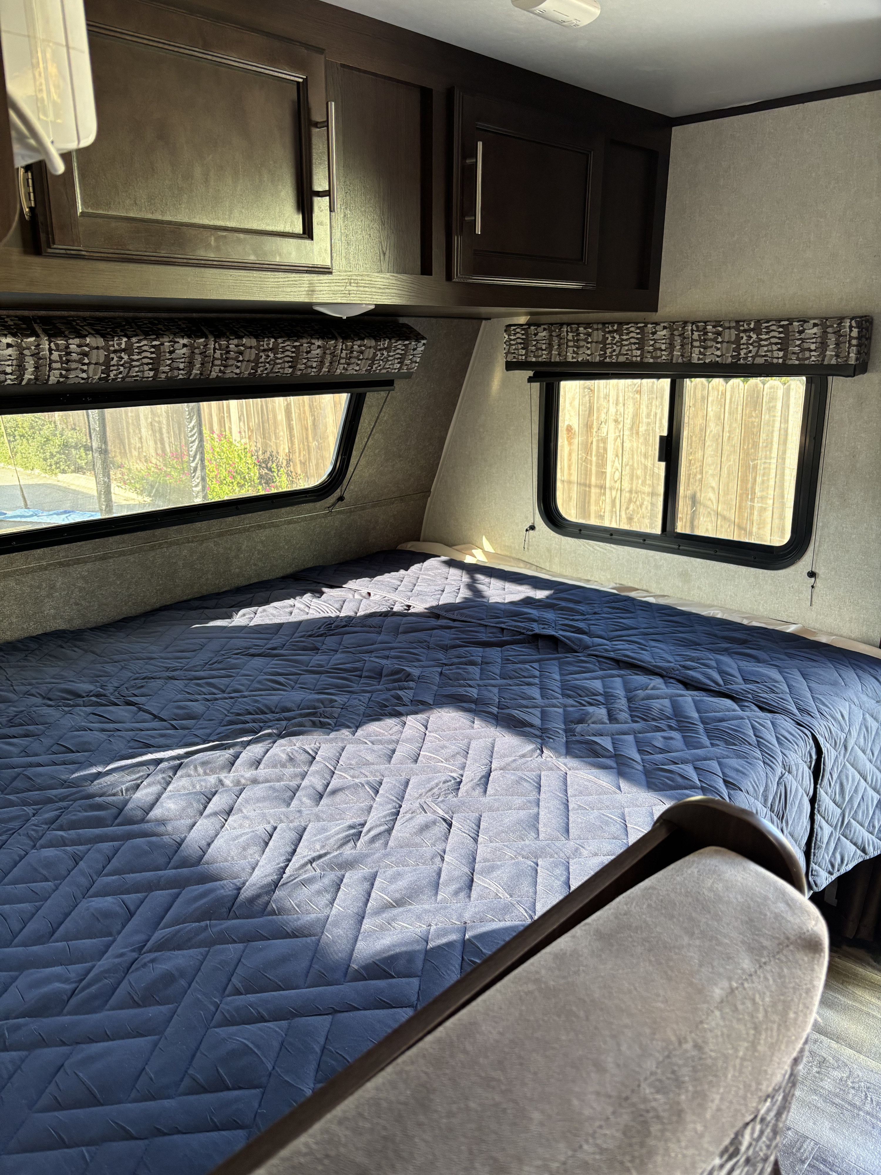 Cozy RV rental bedroom featuring a dark blue quilted bedspread, overhead cabinets, and sunlit windows.. Jayco Jay Flight SLX 2019