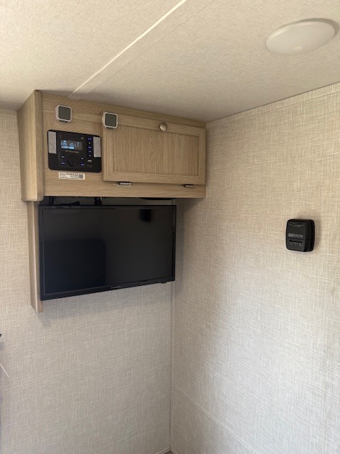 RV rental interior: Overhead entertainment system with a stereo and TV, plus a wall-mounted thermostat, on textured walls.. Forest River Rockwood Geo Pro 2021