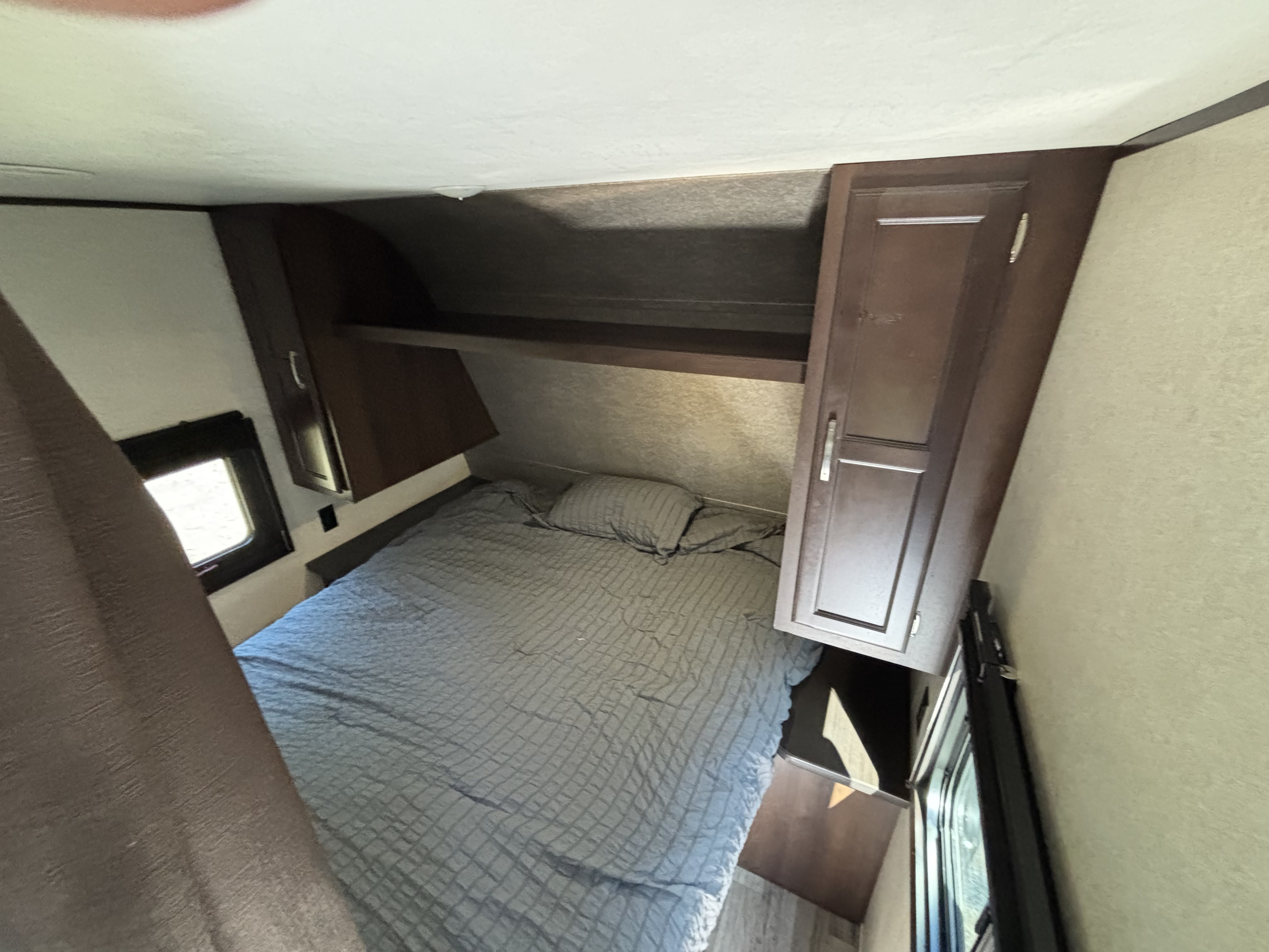 Cozy RV rental bedroom featuring a comfortable bed with overhead storage and windows. Ideal for compact travel.. Jayco Jay Flight 2020