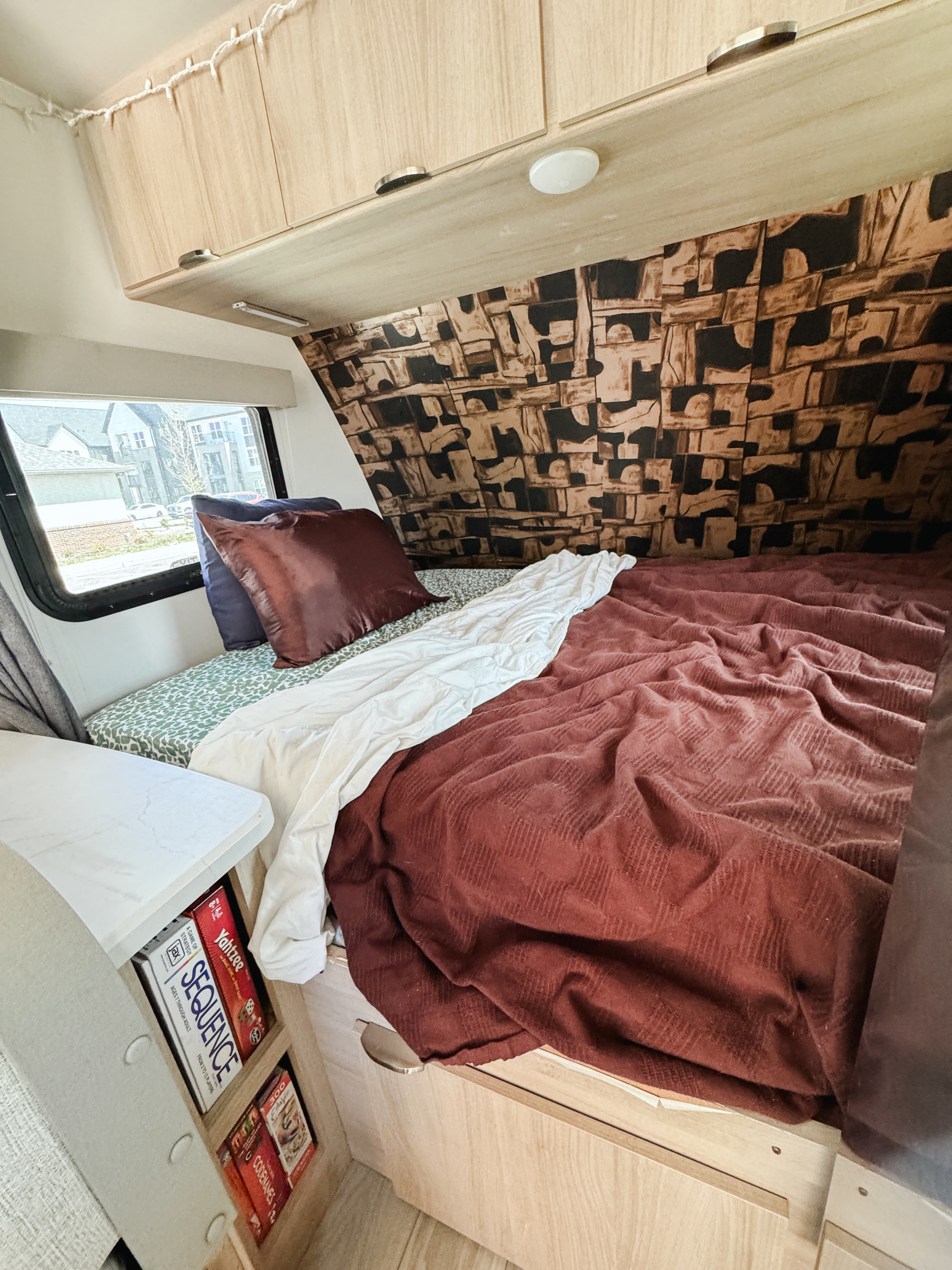 Cozy RV rental bedroom with patterned wall, plush bed, and board games like Sequence & Yahtzee stored below.. Winnebago Micro Minnie Winnie 2023