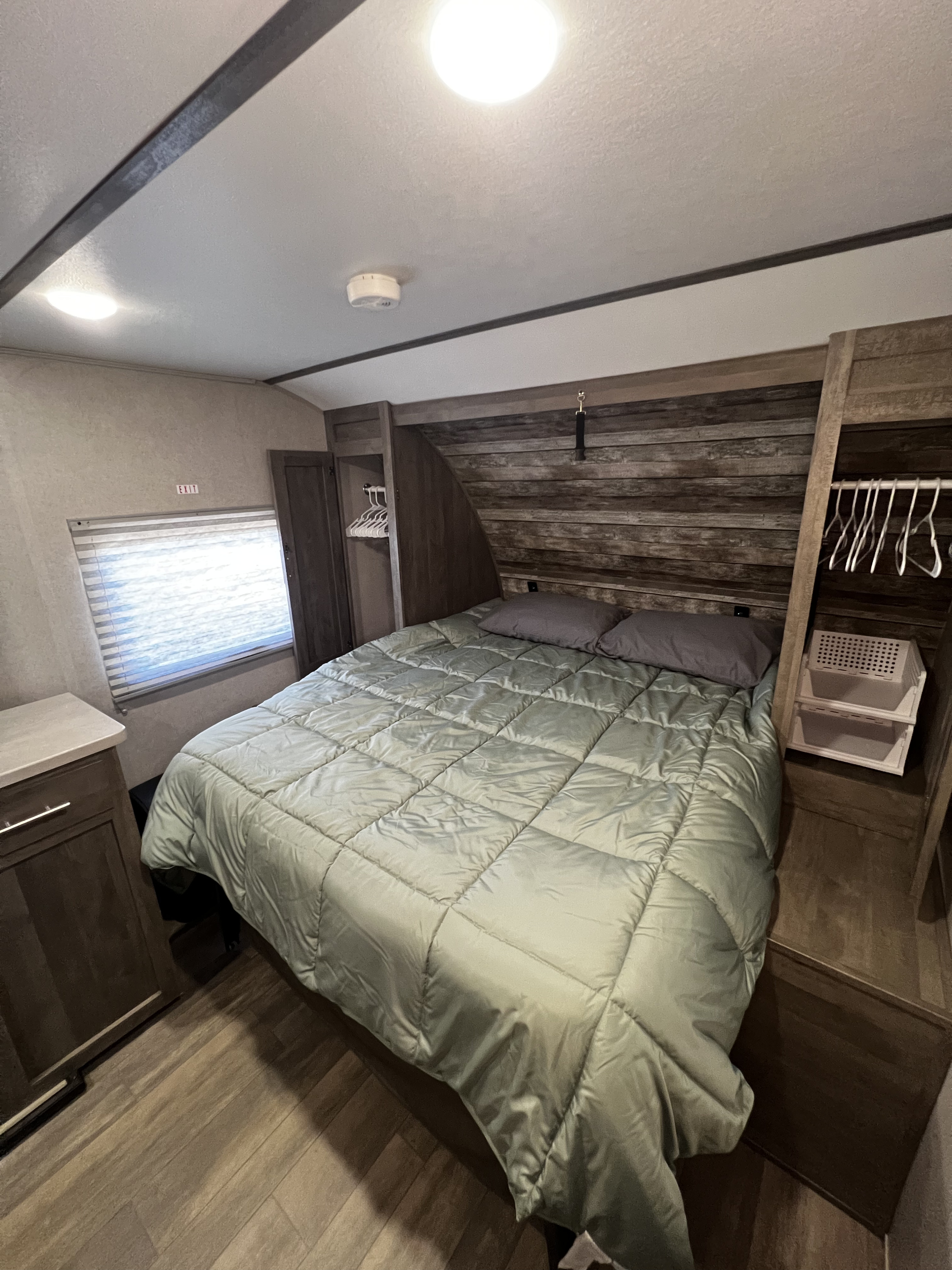 RV rental bedroom: a bed with light green comforter, wood headboard, built-in storage, and a window with blinds.. Forest River XLR Micro Boost 29LRLE 2022
