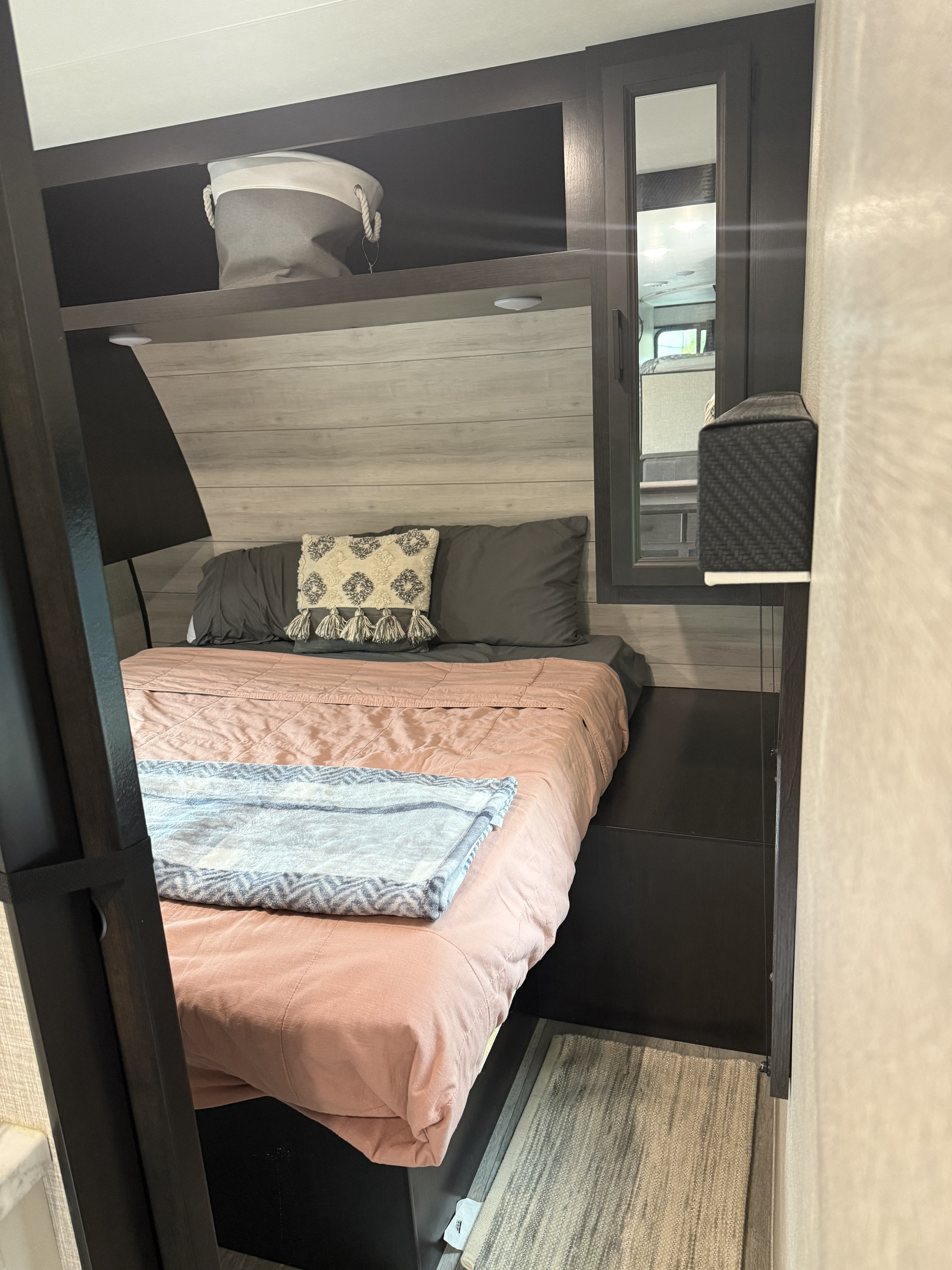Cozy RV rental bedroom with pink bedding, patterned pillows, overhead storage, and mirror. Ready for your next adventure!. Jayco Jay Flight 2023