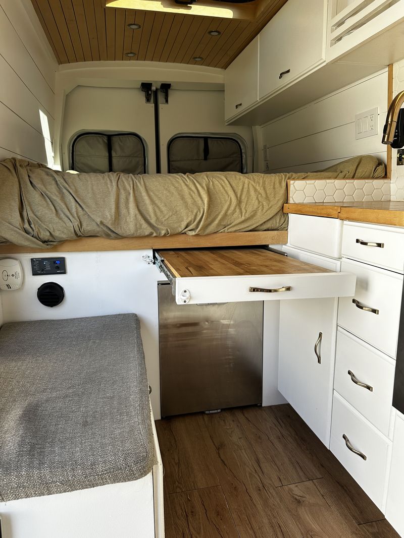 Comfortable RV rental camper van interior. Features a bed, compact kitchen with pull-out counter, fridge, and ample storage.. Ford Transit 2019
