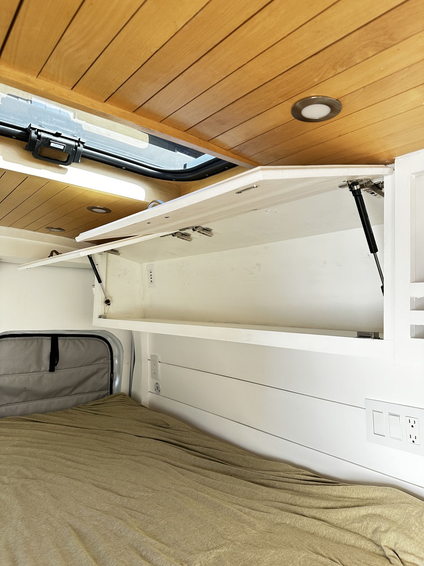 Cozy rv rental interior featuring a wooden ceiling, open overhead storage, a bed, lights, and power outlets.. Ford Transit 2019