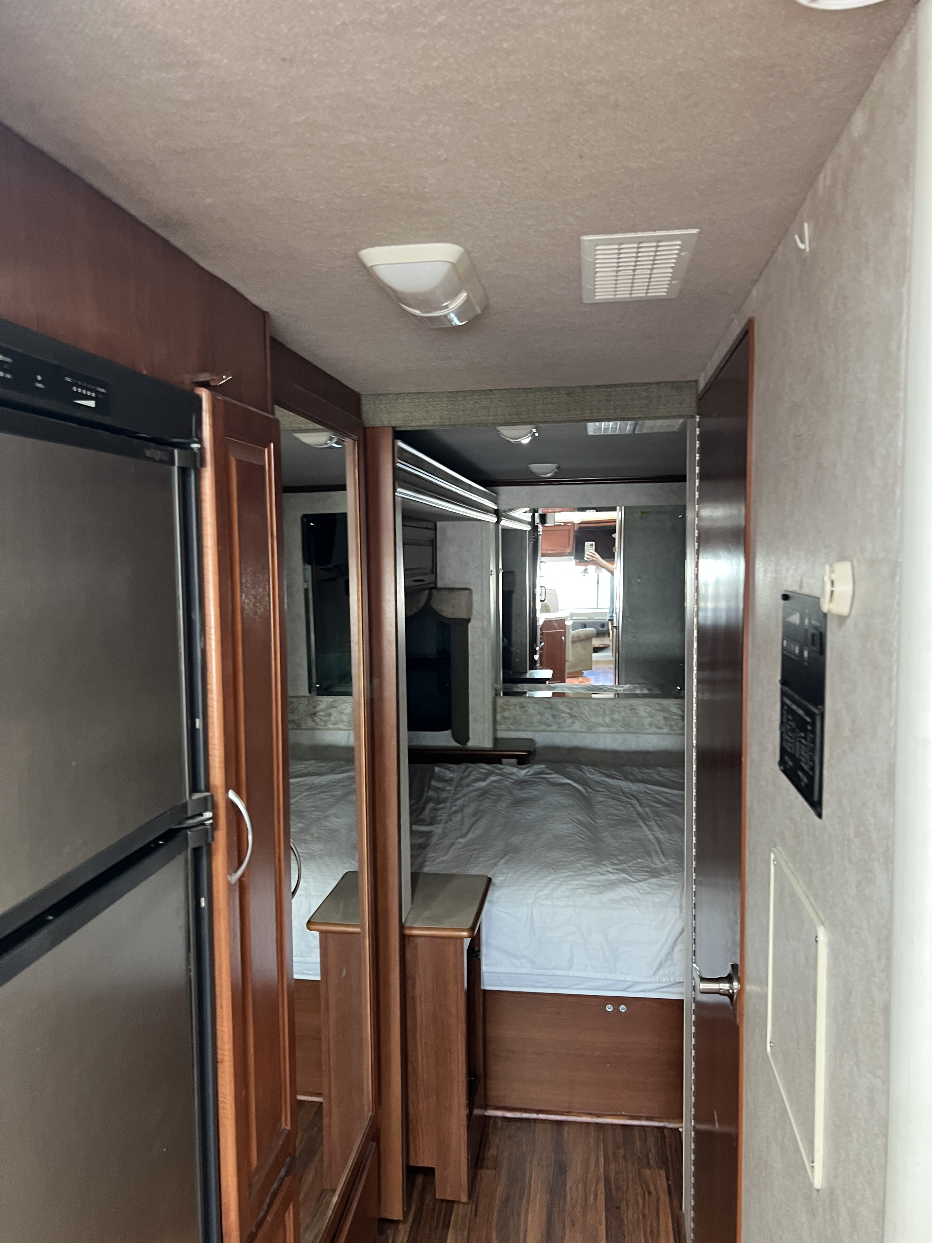 Inside an RV rental, a compact hallway leads past a fridge to a neatly made bed in the bedroom area, reflecting a spacious feel.. Southwind Southwind Motorhome 2003