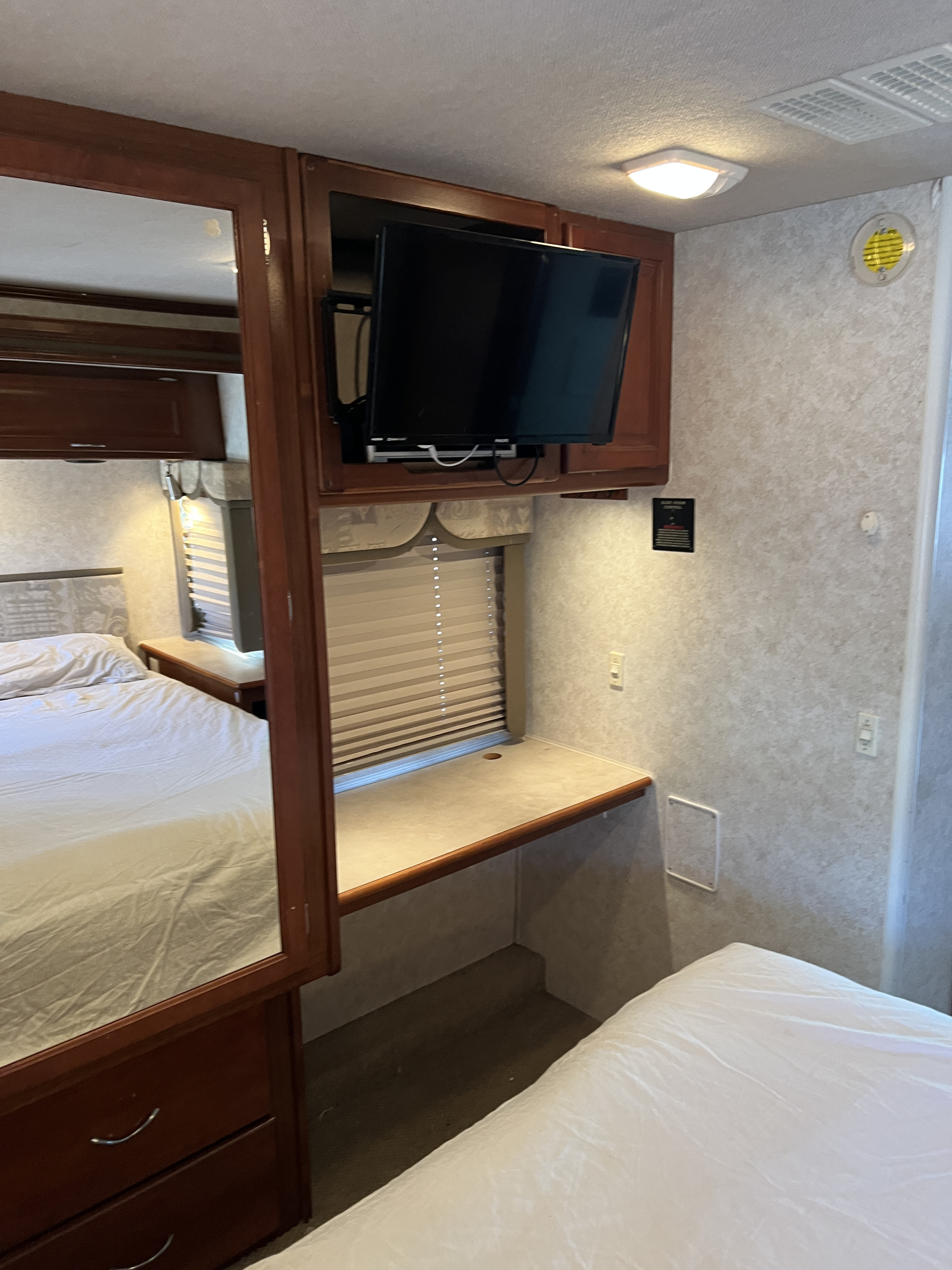 This RV rental bedroom offers a comfortable bed, mirror, TV, and desk space. Perfect for travel comfort.. Southwind Southwind Motorhome 2003