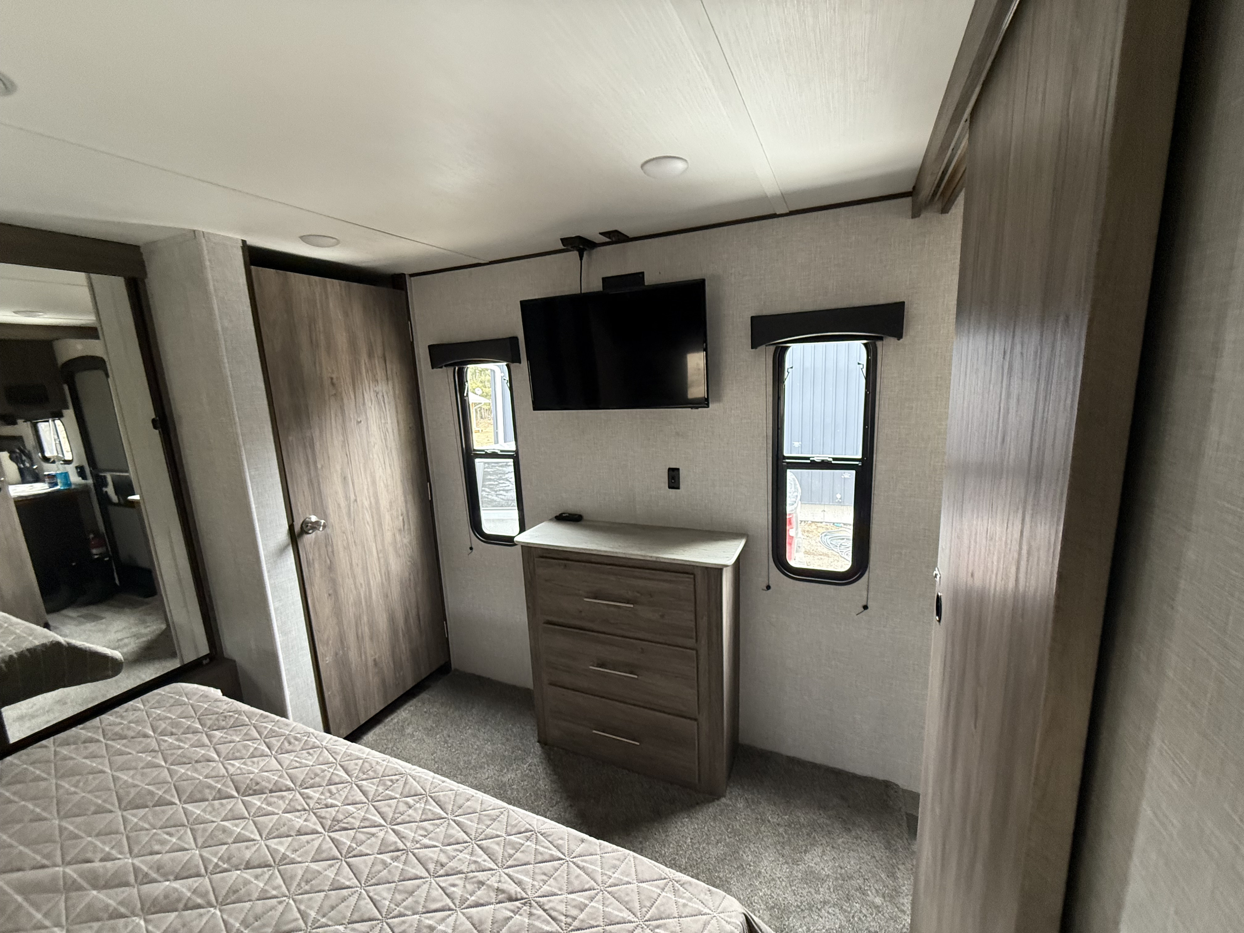 Inside an RV rental, this clean bedroom features a mounted TV, dresser, and windows, offering comfort on the road.. Crossroads Zinger 2025
