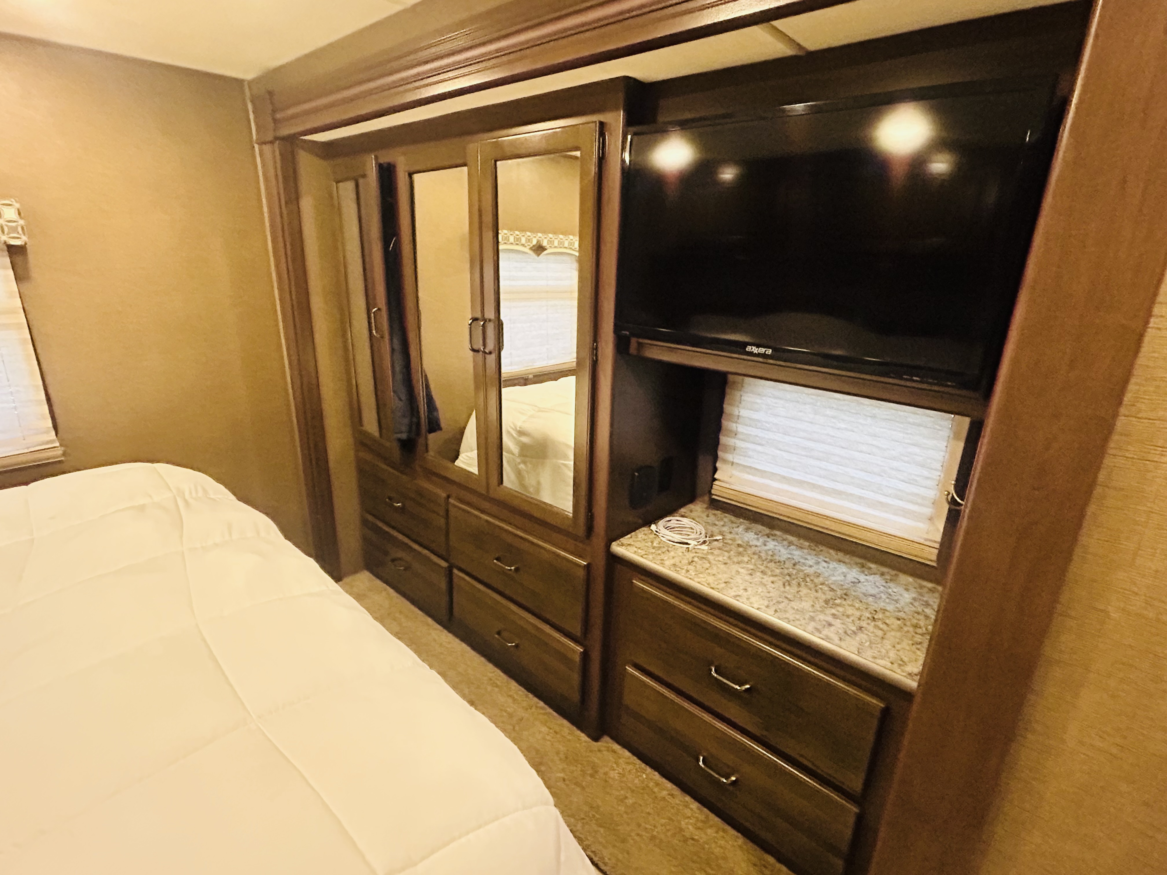 Spacious RV rental bedroom featuring a comfortable bed, built-in wardrobe, dresser, and TV for a cozy stay on the road.. Thor Hurricane 2018