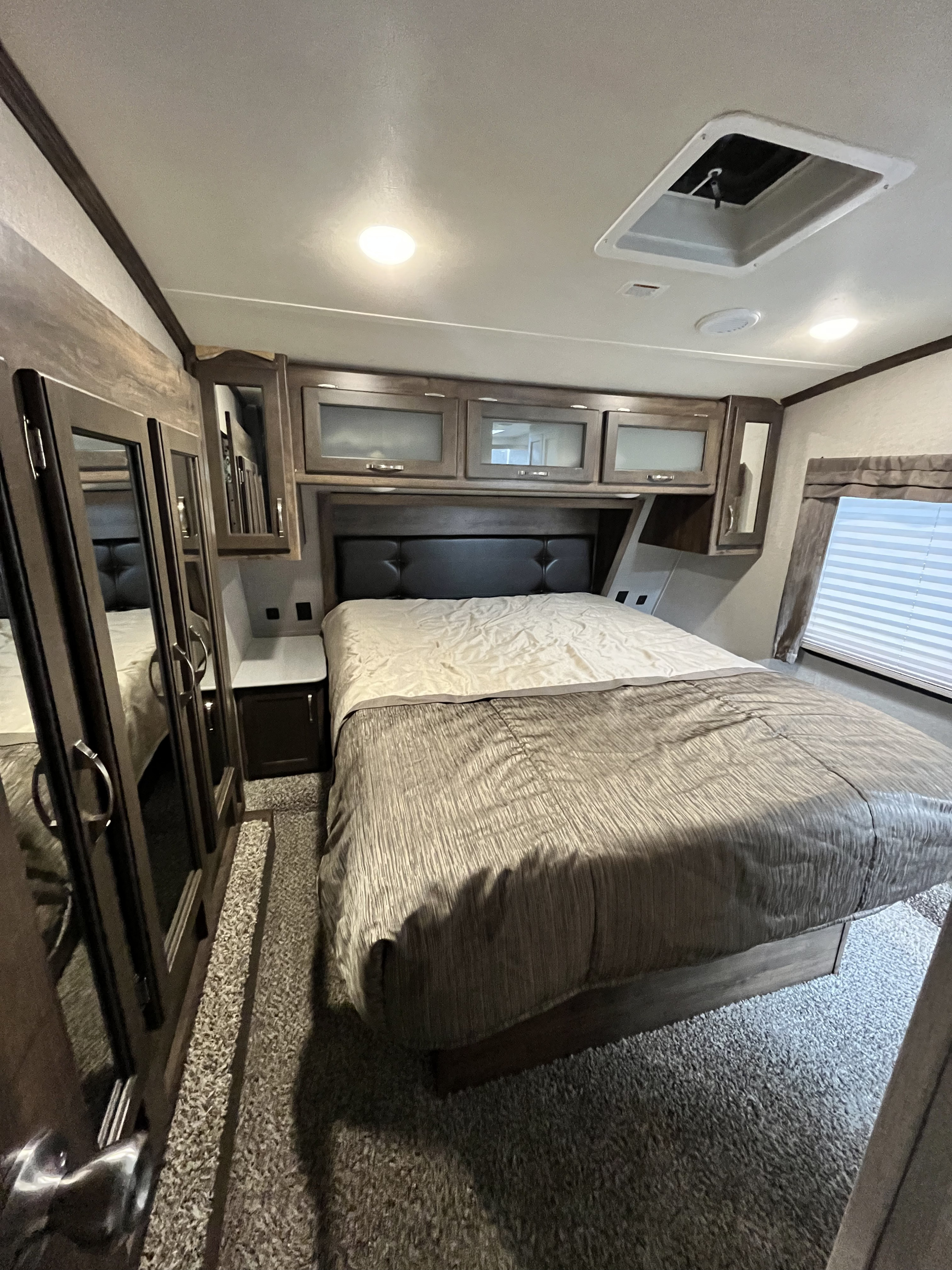 Explore this inviting RV rental bedroom featuring a queen bed, overhead cabinets, and mirrored wardrobes for a comfortable stay.. Dutchmen Astoria 2018
