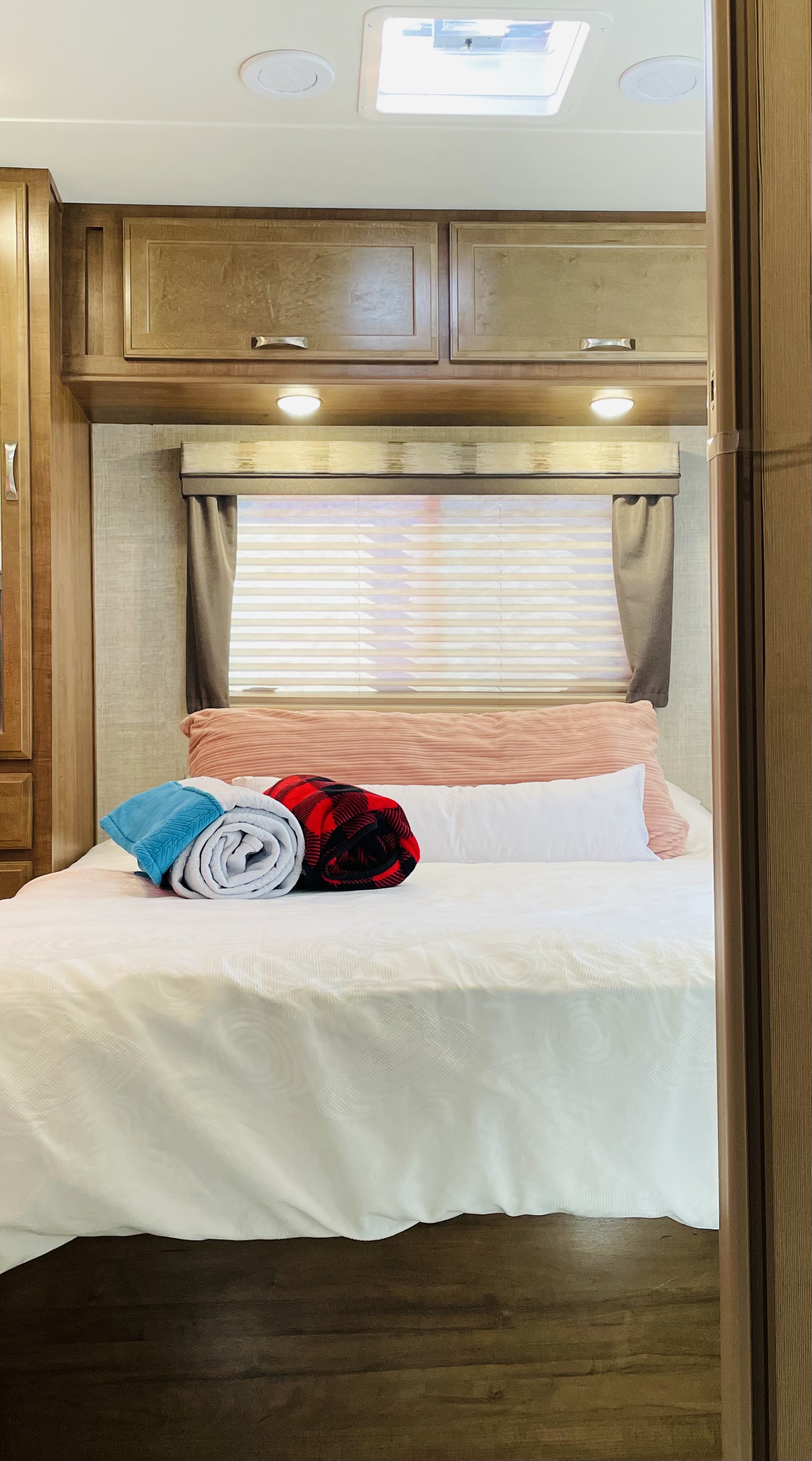 An inviting RV rental bedroom with a comfy bed, colorful blankets, wood cabinets, and window.. Gulf Stream Conquest 2020