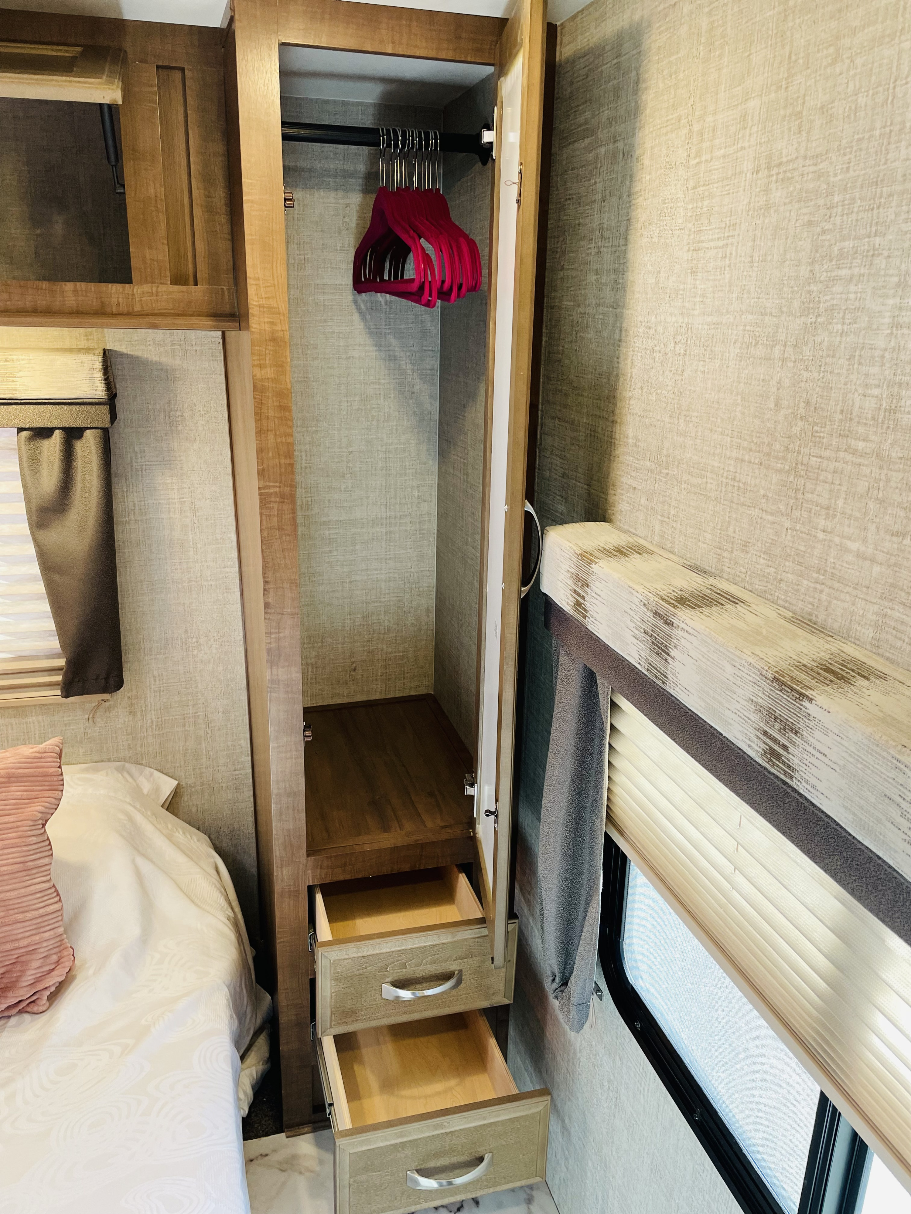 RV rental bedroom with open closet showing pink hangers, pull-out drawers, and a window with blinds.. Gulf Stream Conquest 2020