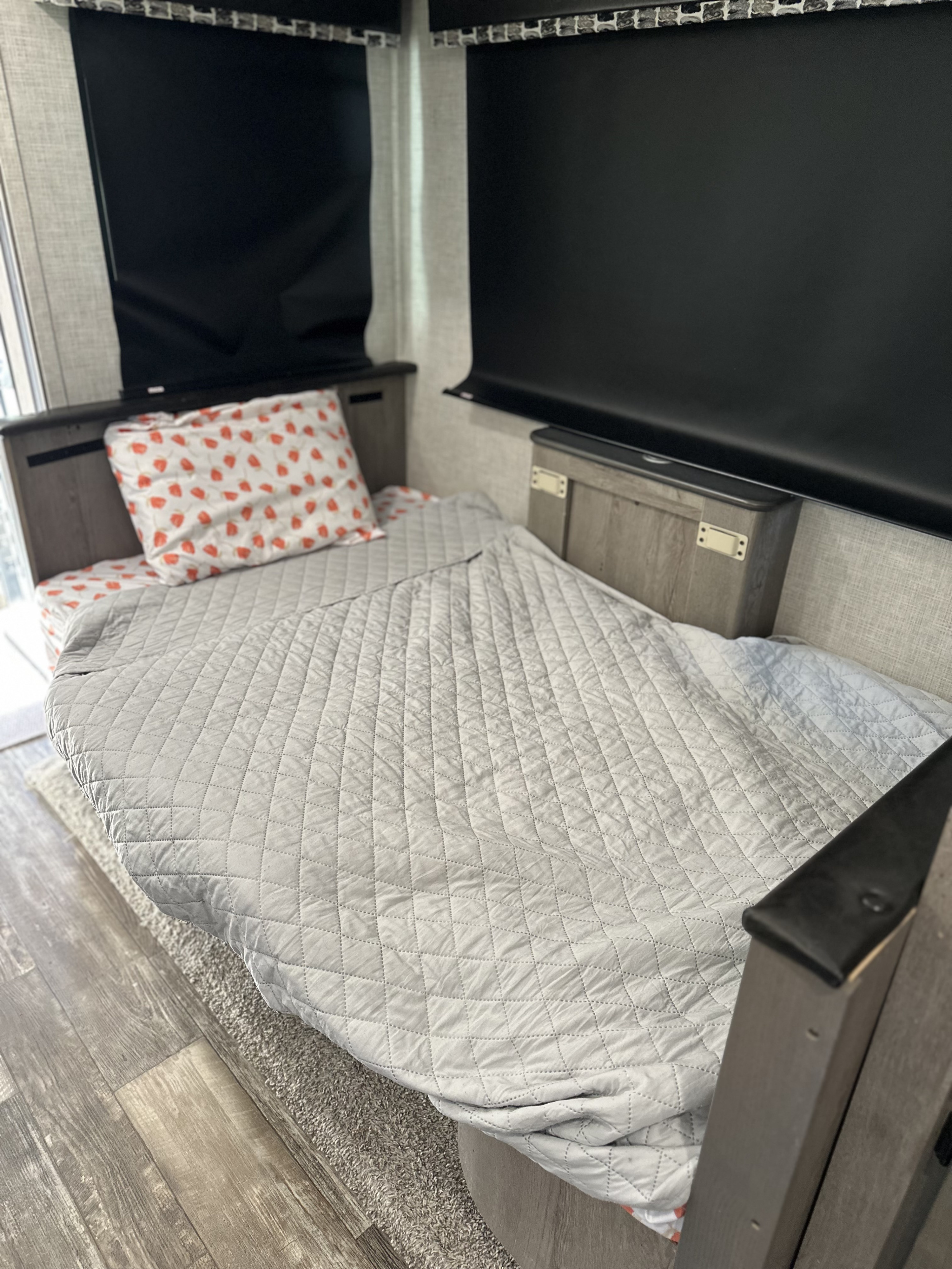 Cozy RV rental bed with a grey quilted blanket and a white, red-strawberry patterned pillow, ideal for relaxing.. Keystone RV Outback 2019