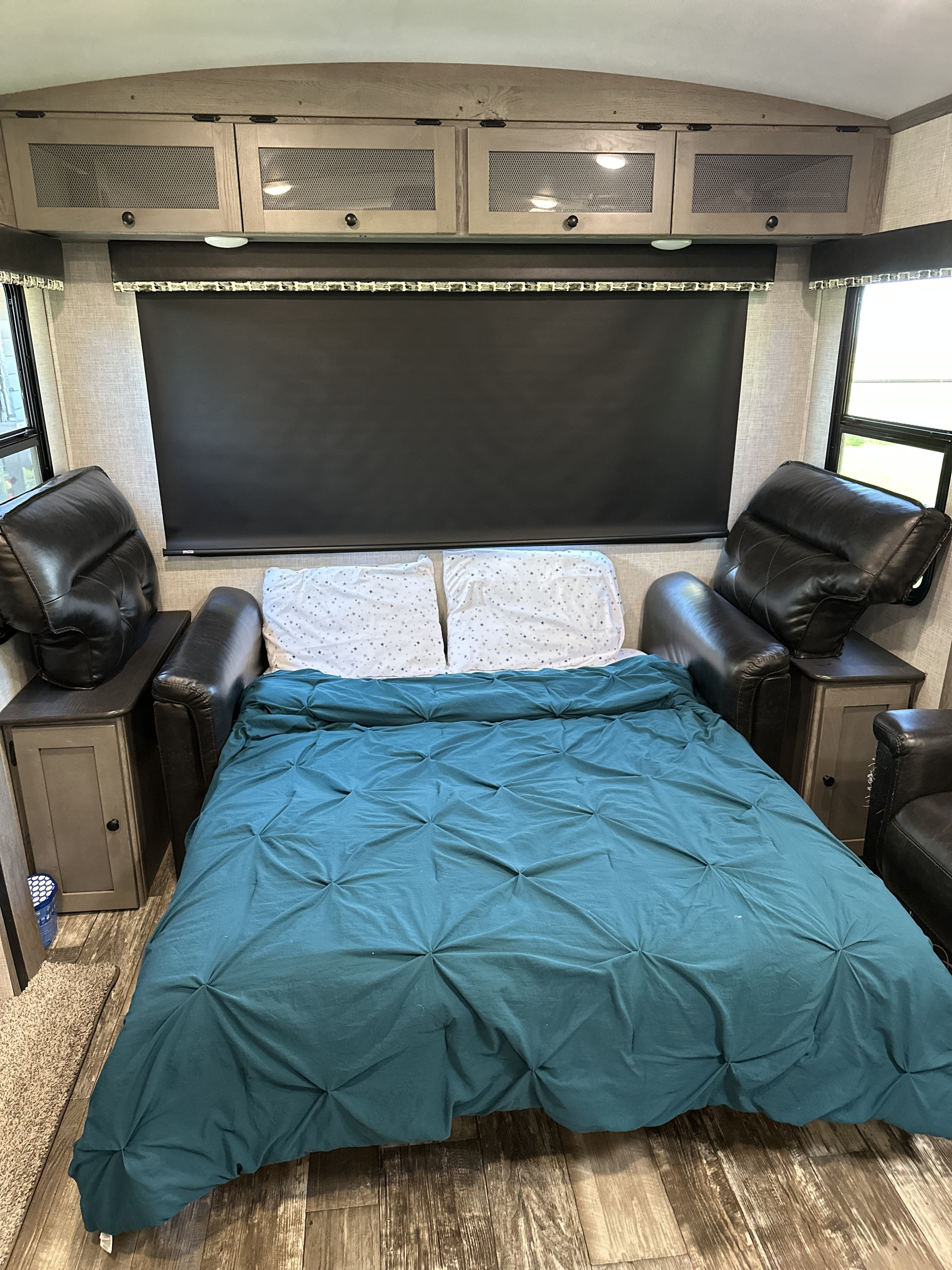 Cozy RV rental bedroom with teal bed, black leather recliners, and light wood cabinets, ideal for travel.. Keystone RV Outback 2019