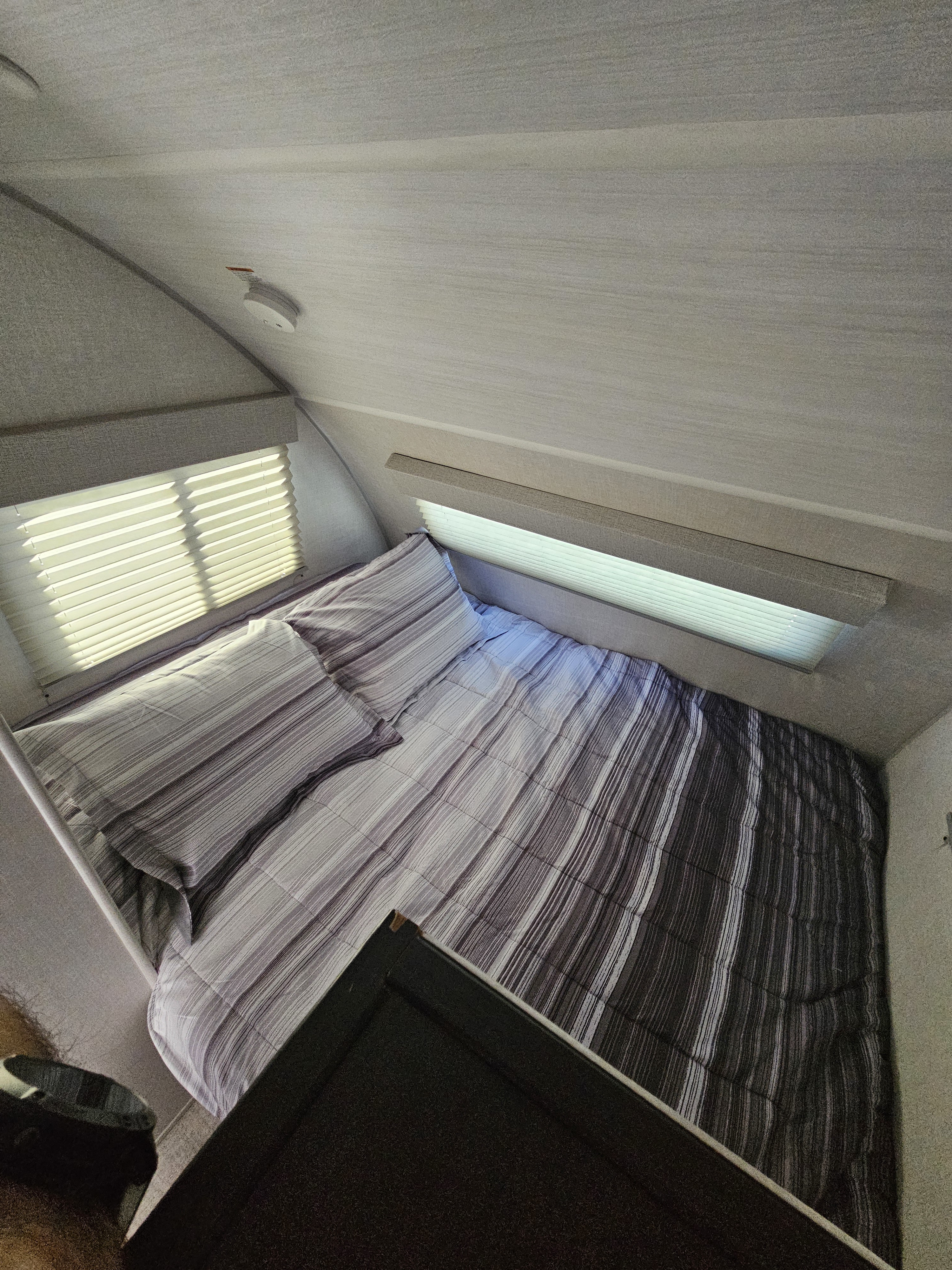 Inside an RV rental: a bright, cozy sleeping area with striped gray bedding, windows with blinds, and curved walls.. Forest River R-POD 171C 2024