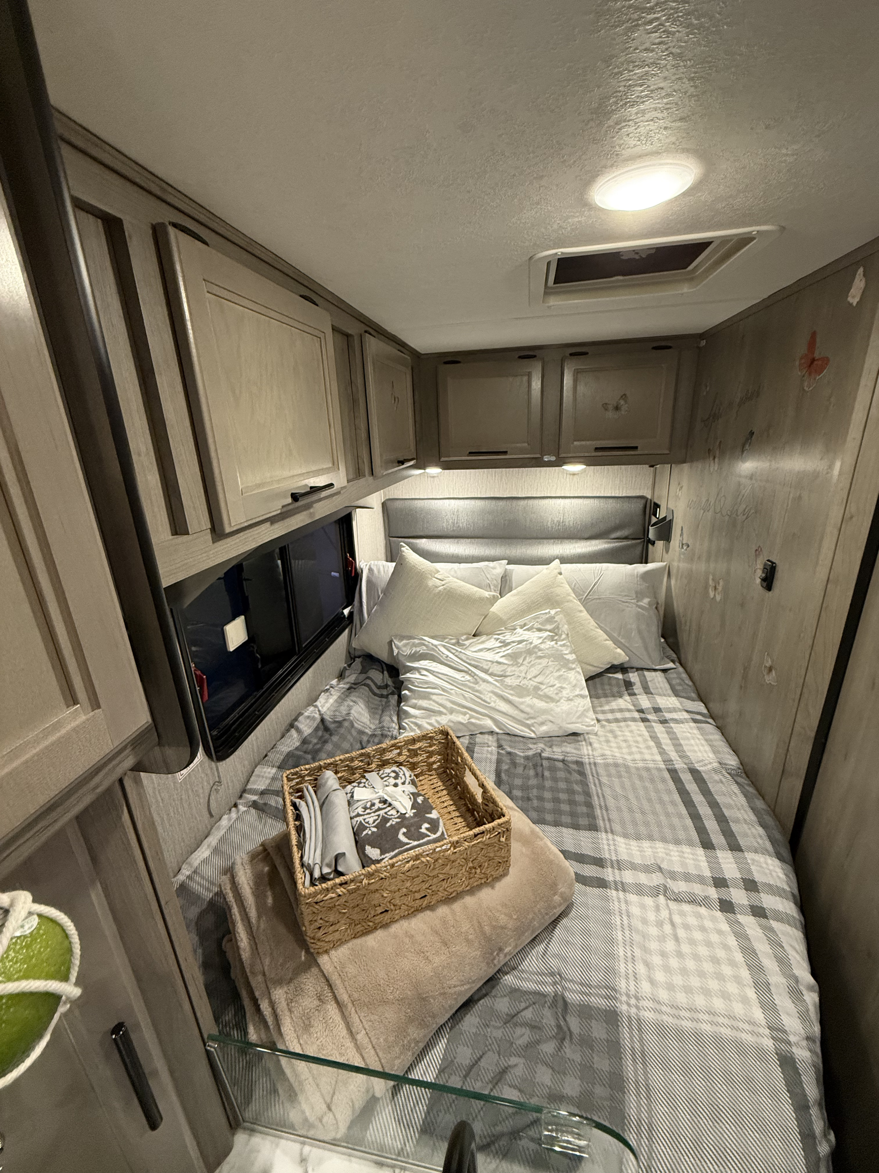 Cozy RV rental bedroom featuring plaid bedding, overhead cabinets, a comfortable headboard, and a basket of amenities.. Coachmen Cross Trail 20 CBT 2022