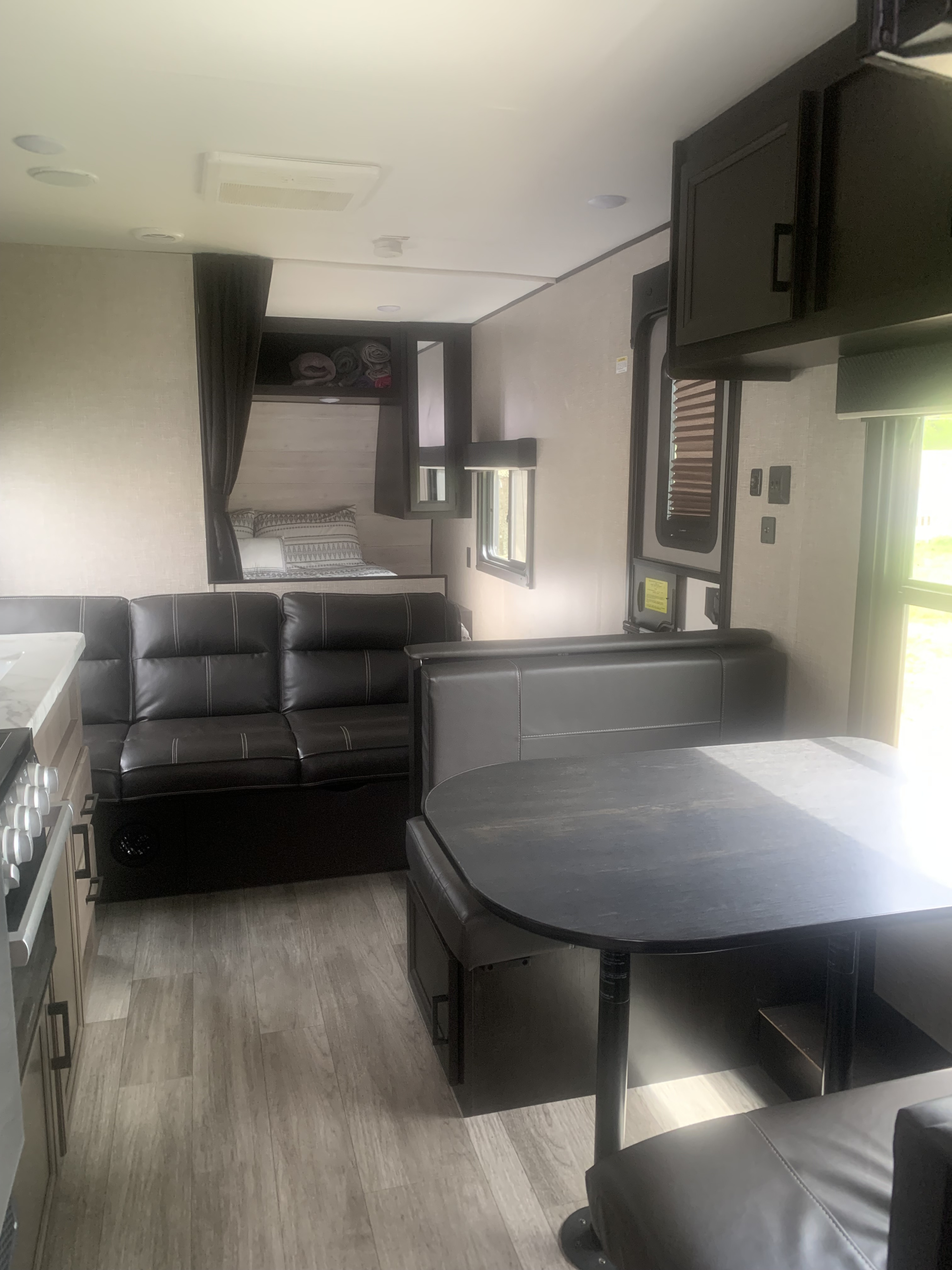 View inside an RV rental showing a kitchen, black sofa, bunk beds, and a dark dining table with seating.. Jayco Jay Flight 2023