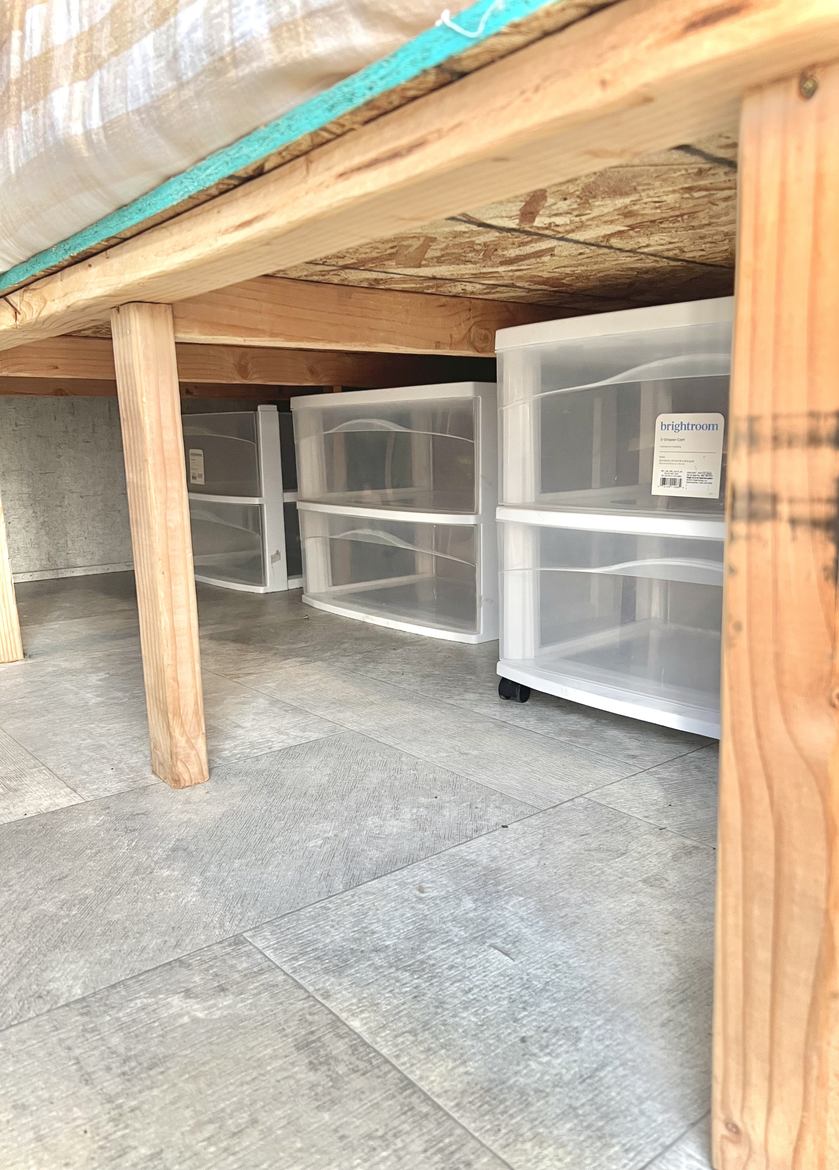 Under-bed storage in an RV rental: clear plastic drawers are neatly organized on a grey floor, seen from a low angle under wooden beams.. Coachmen 226 BH 2019