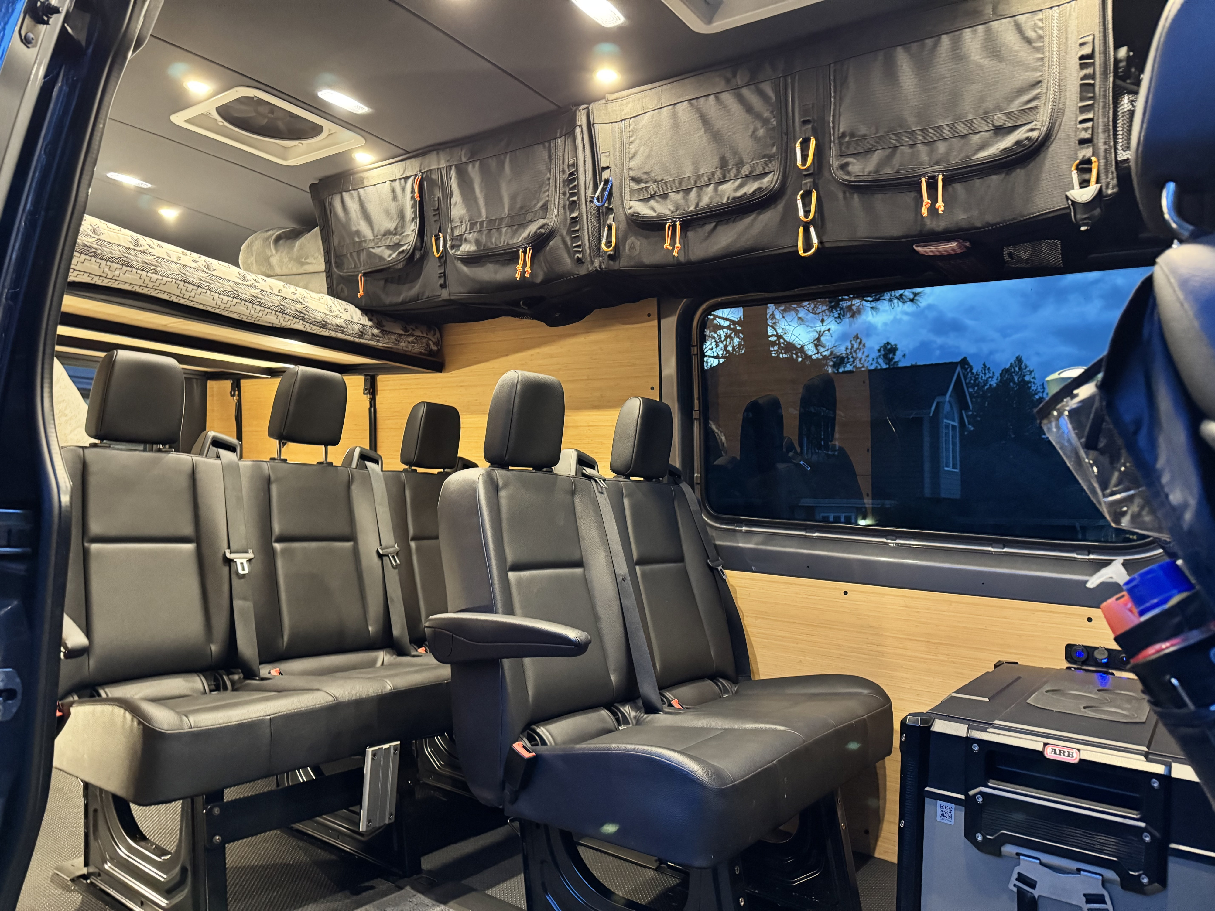 Inside a custom RV rental camper van, showing comfortable passenger seating, overhead storage, and a raised bed.. Mercedes Benz Sprinter 2022