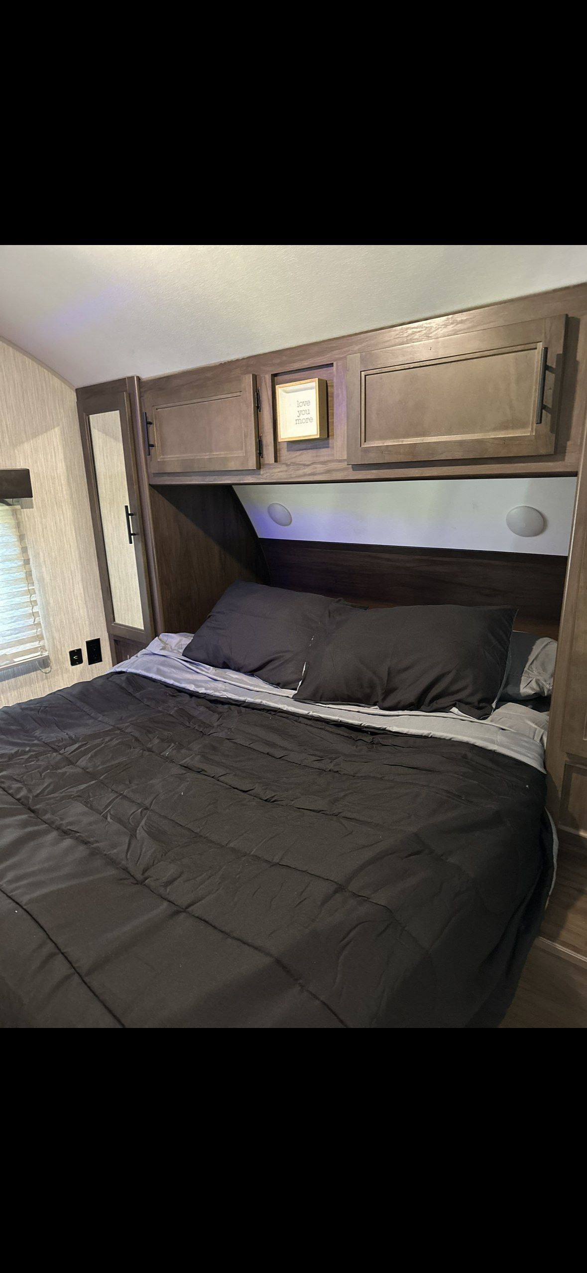 Cozy RV rental bedroom with dark bedding, wooden overhead cabinets, and a mirrored closet. Perfect for travel comfort.. Forest River Cherokee Grey Wolf 2020
