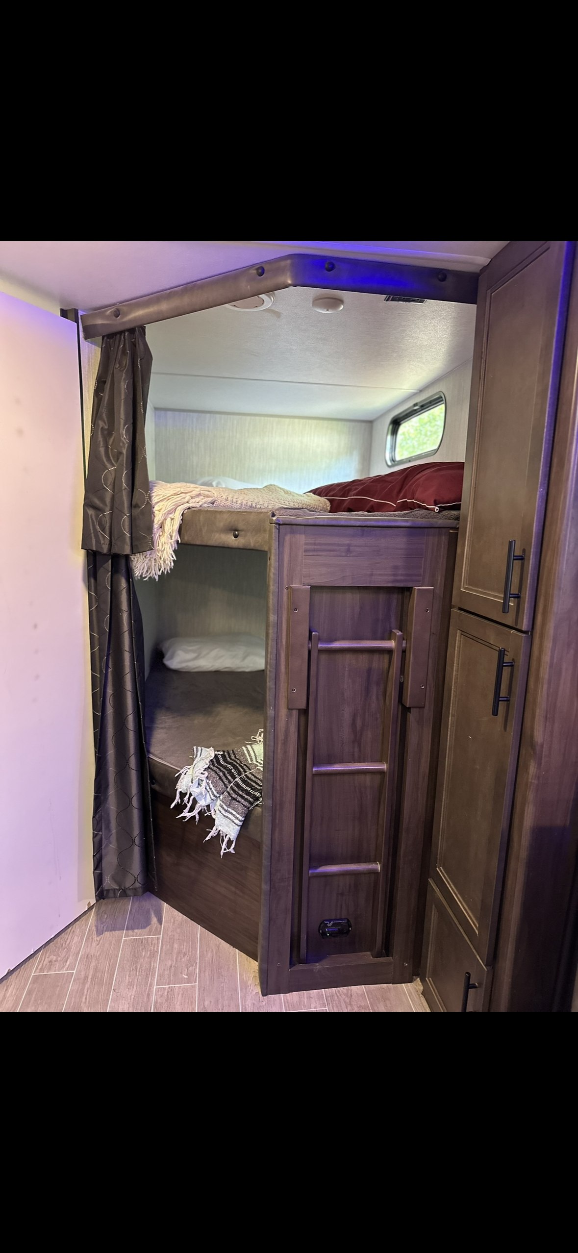 Inside an RV rental, dark wood bunk beds with privacy curtains and a folded ladder beside cabinets, offering compact sleeping.. Forest River Cherokee Grey Wolf 2020