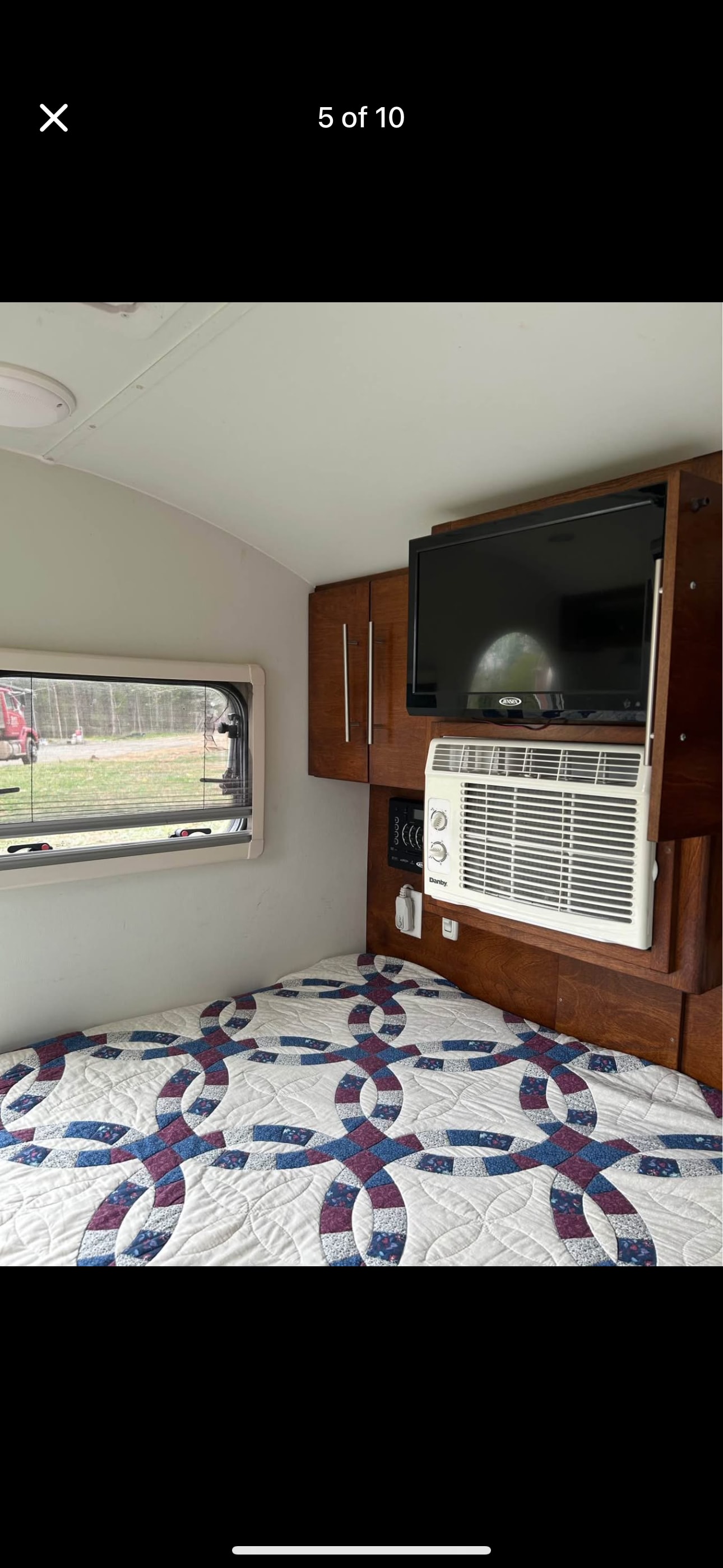 Cozy RV rental interior with a patterned quilt on the bed, wall-mounted TV, AC unit, and wooden cabinets.. nuCamp T@G 2018
