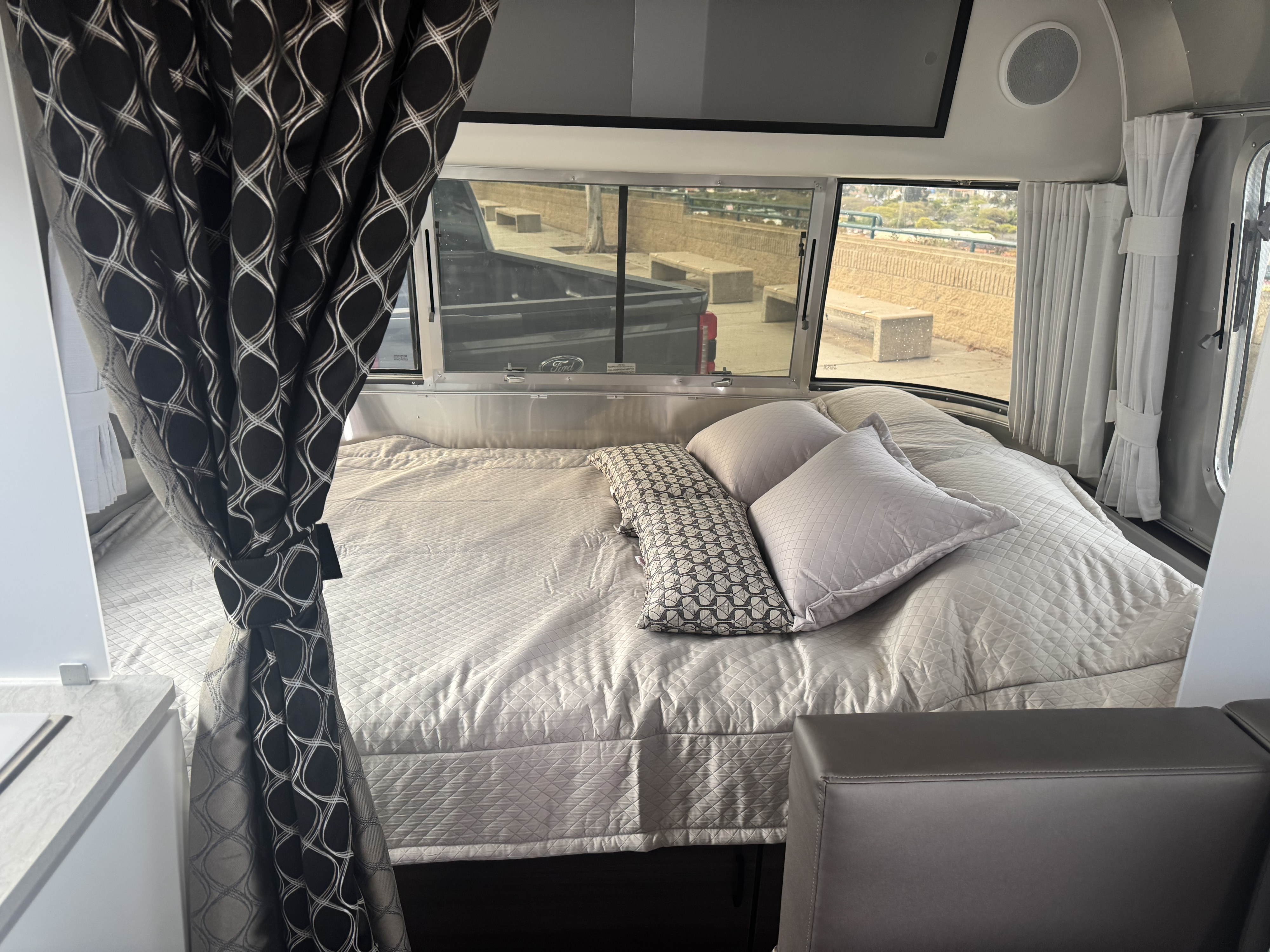 Cozy rv rental interior with a quilted bed, stylish patterned curtains, and scenic outdoor views from the large windows.. Airstream 22' Airstream Caravel 2025