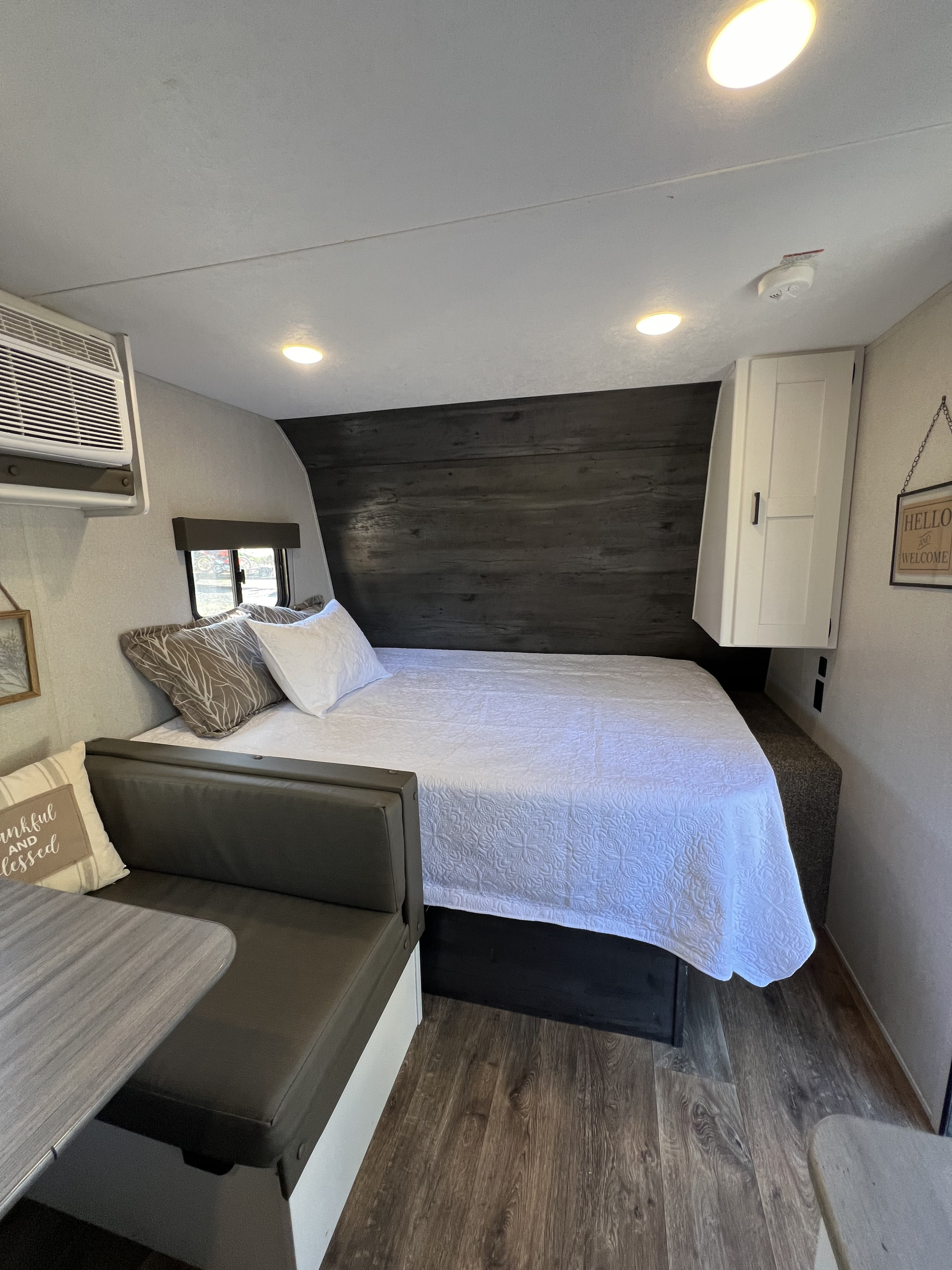 Modern RV rental's bedroom & dining area, featuring a bed with white quilt, AC, and a cozy bench with a table.. Keystone RV Hideout 2021
