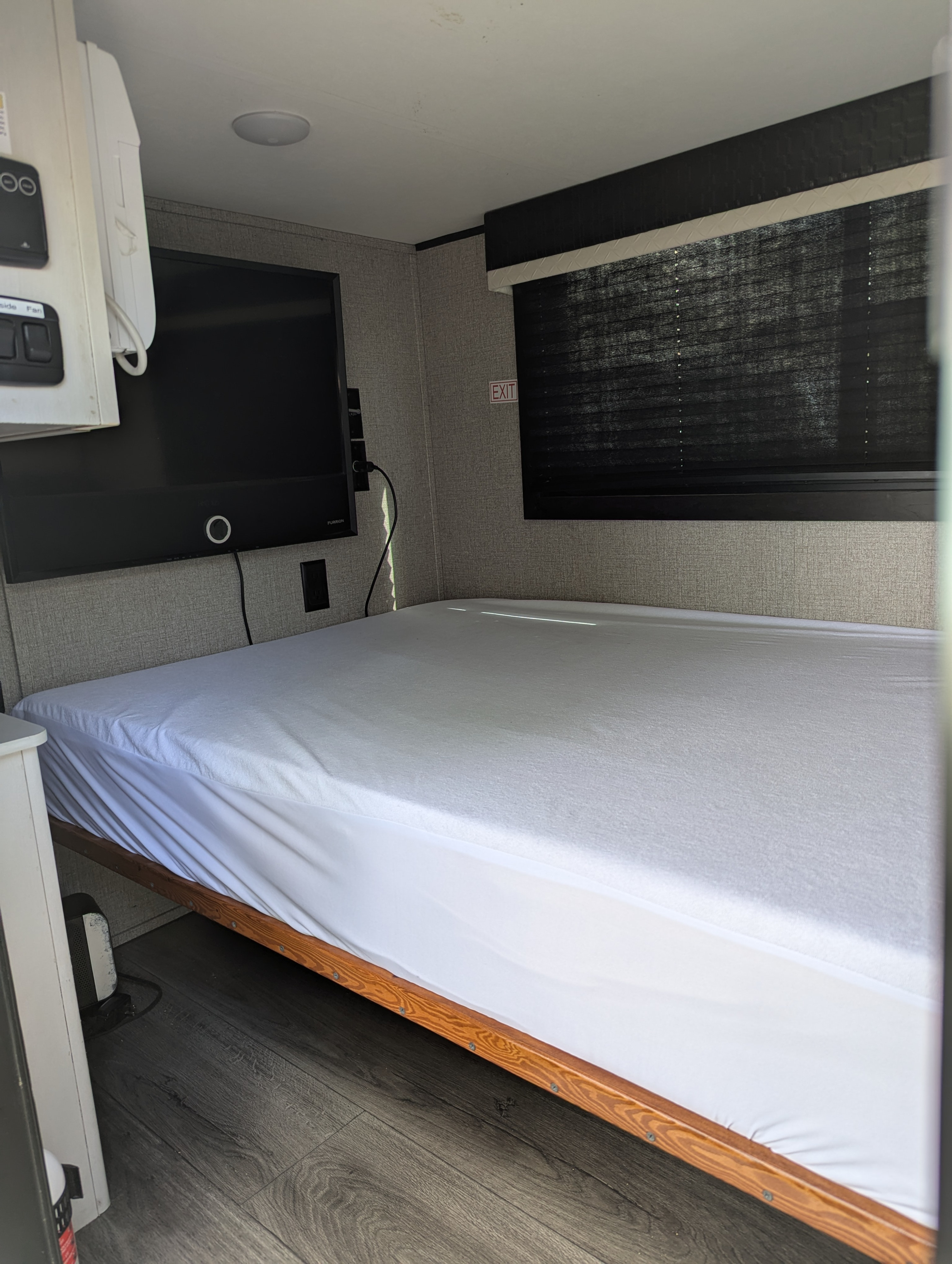 Compact RV rental bedroom with white bed, wall-mounted TV, and window blinds, ready for travel.. Jayco Jay Feather Micro 12SRK 2021