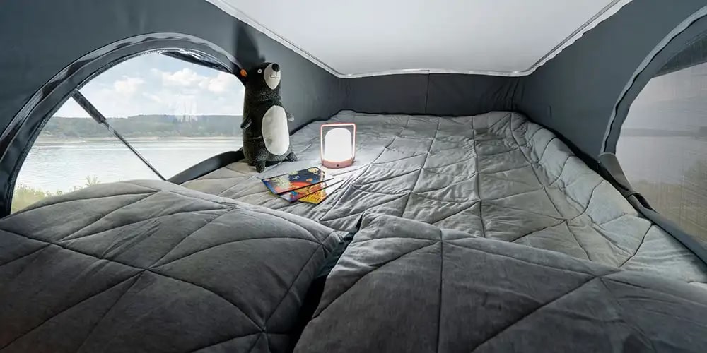 Cozy RV rental sleeping area: a comfortable pop-top bed with a scenic lake view, plush toy, and soft lamp.. Winnebago Solis 2025