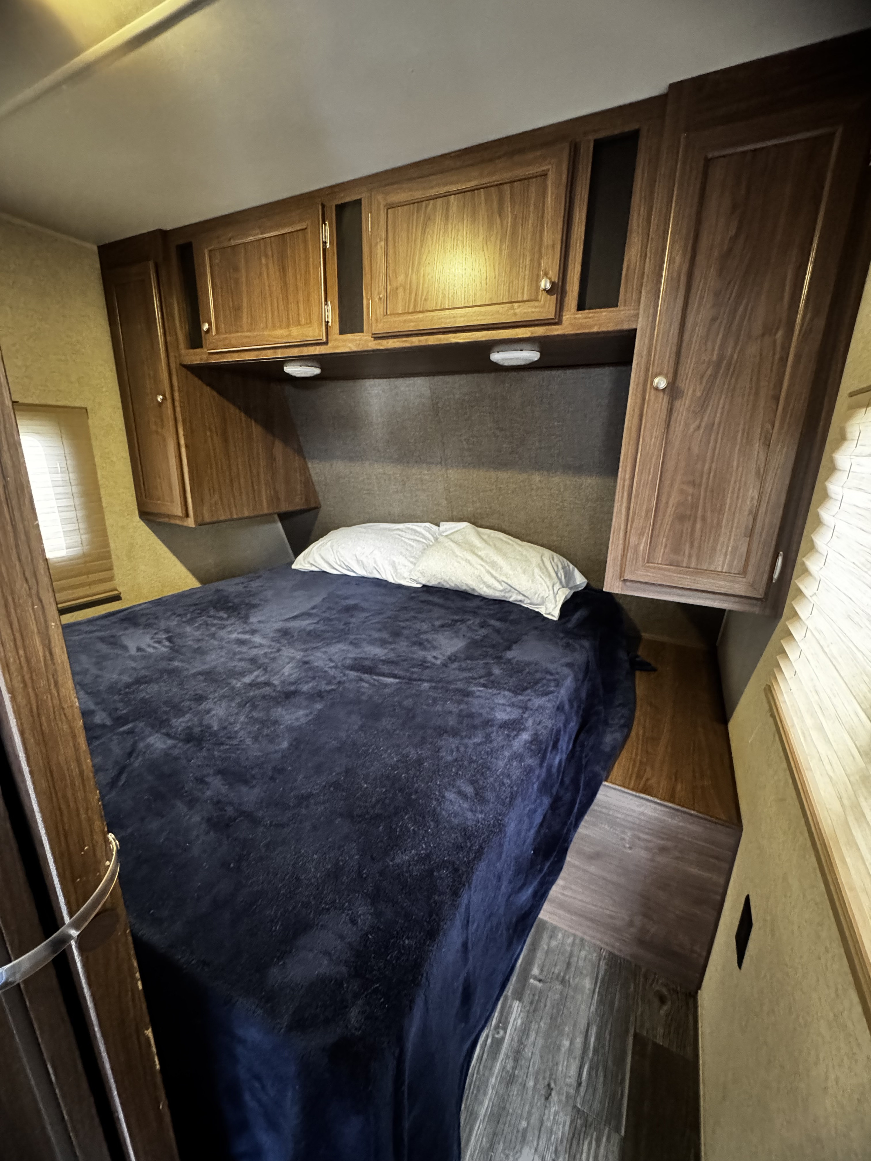 RV rental: A cozy bedroom features a bed with a dark blue blanket, pillows, overhead wooden cabinets, and a window.. Heartland Pioneer 2016