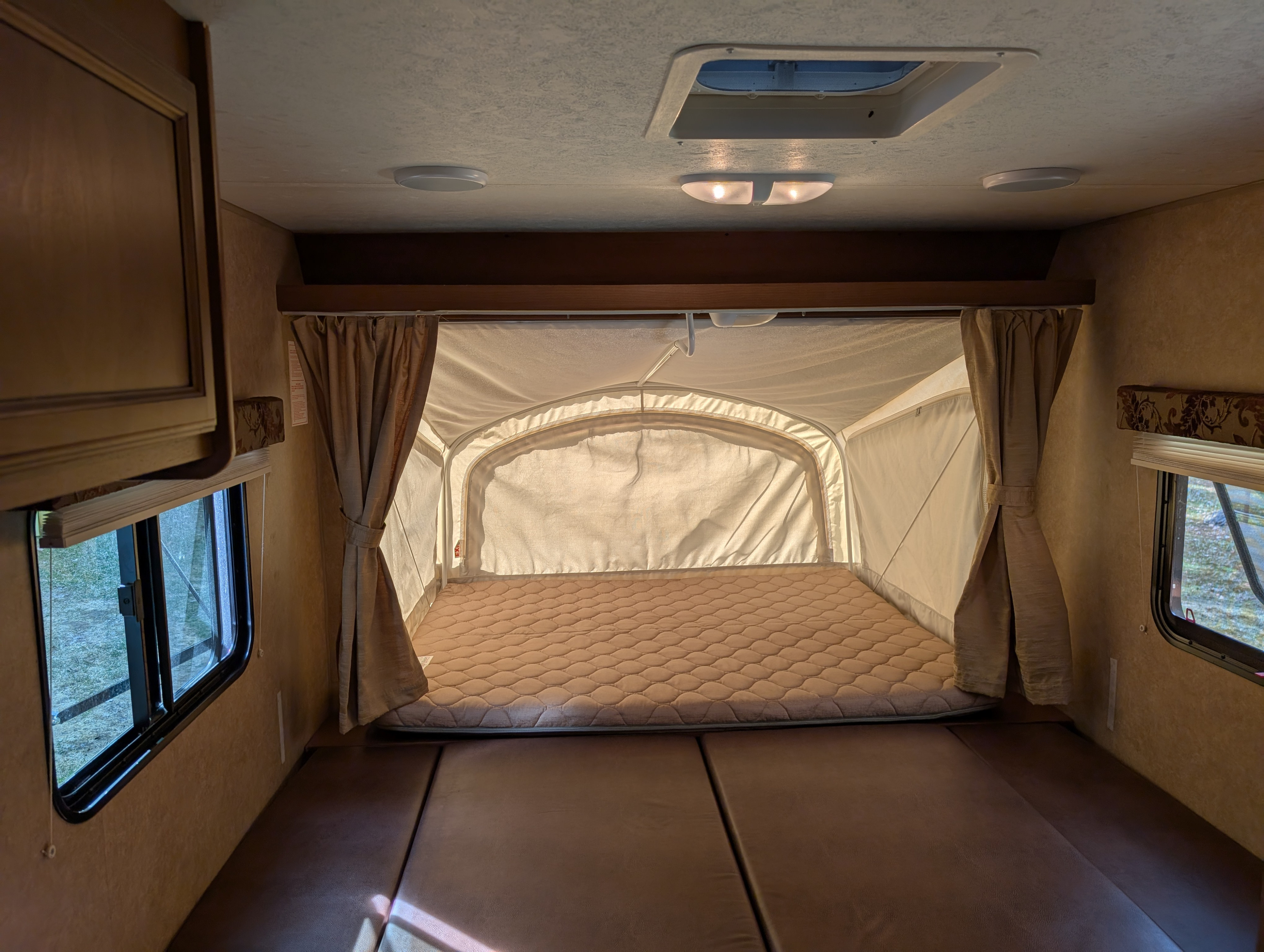 RV rental interior: large pop-out bed with quilted mattress & brown seating. Windows show the outdoors.. Starcraft AR-One 2014