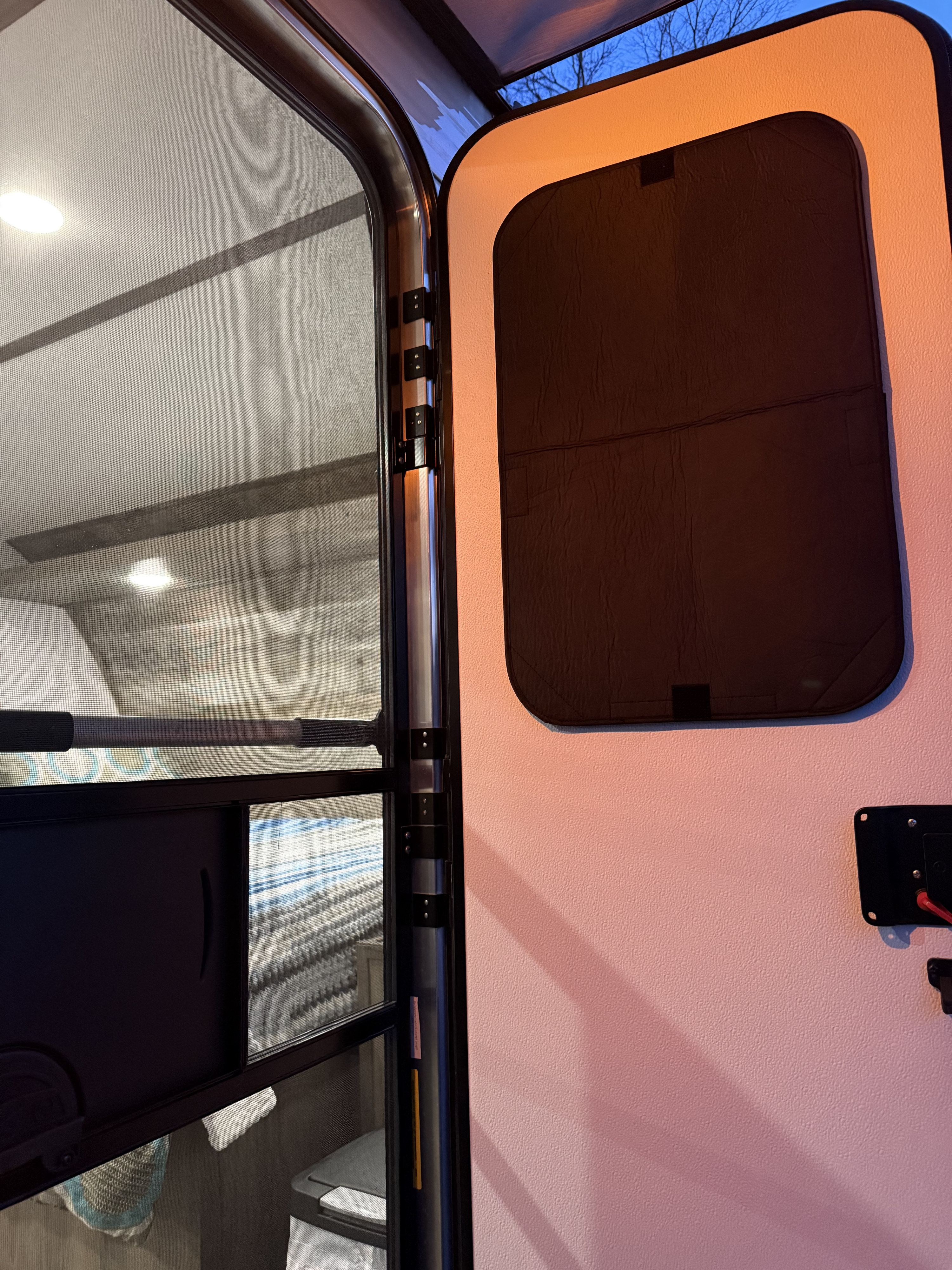 Inside an RV rental: An open screen door reveals the camper's cozy interior and a glimpse of the blue sky outside.. Gulf Stream Enlighten 2022