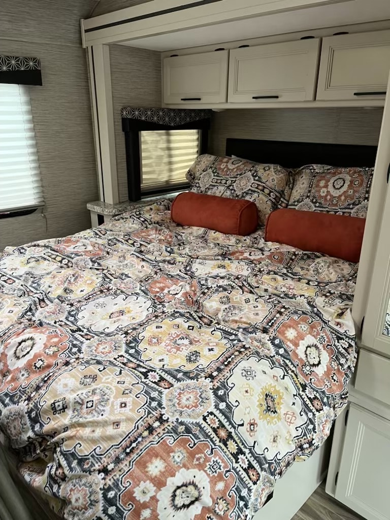 A vibrant RV rental bedroom showcasing a patterned bed with two orange pillows, white cabinets, and window blinds.. Thor Freedom Elite 2022