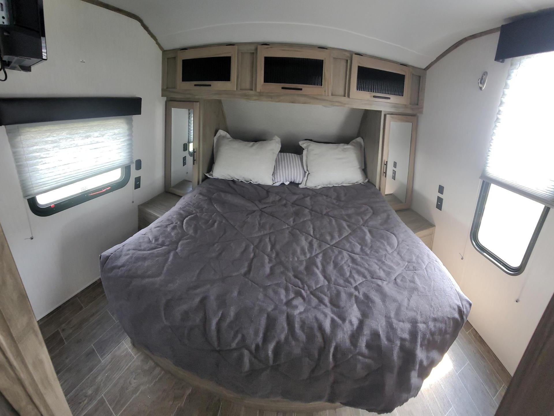Cozy RV rental bedroom interior featuring a bed, overhead cabinets, windows, and mounted TV.. Forest River Cherokee Alpha Wolf 2021