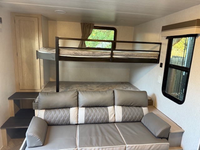 This RV rental's interior features an upper bunk bed, a lower sleeping platform, a comfortable gray sofa, and storage steps.. Forest River Salem 2024