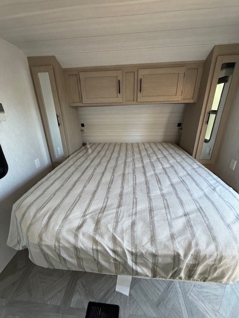 Comfortable RV rental bedroom features a striped bed, light wood overhead cabinets, and compact built-in storage.. Forest River Salem 2024