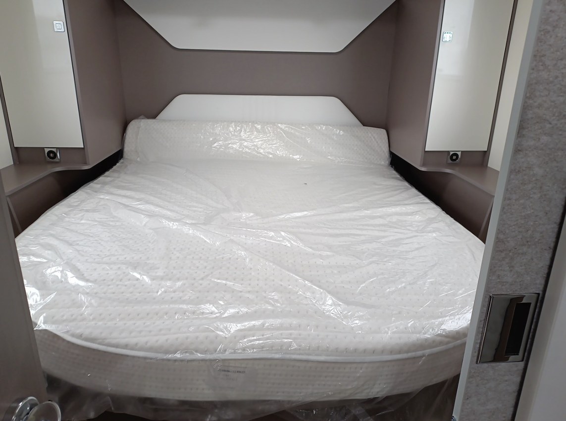Inside an RV rental: new mattress in plastic wrap. Compact bedroom with built-in storage and headboard.. BURSTNER Lyséo TD 736 Privilège 2023