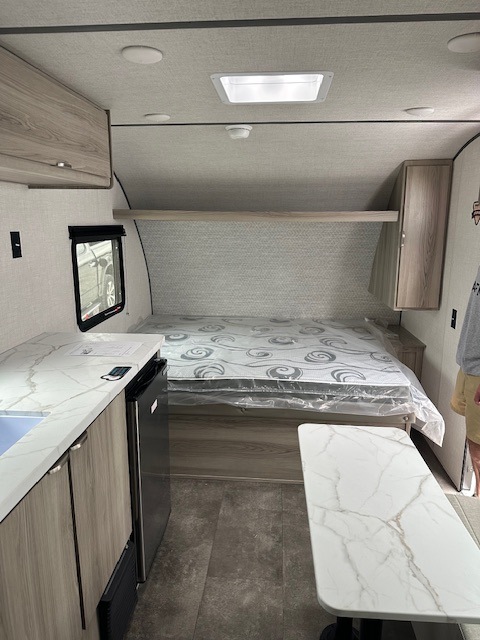 Explore this cozy RV rental interior: bed with plastic cover, kitchenette, and table. Ideal for compact adventures.. Forest River Wildwood 2025