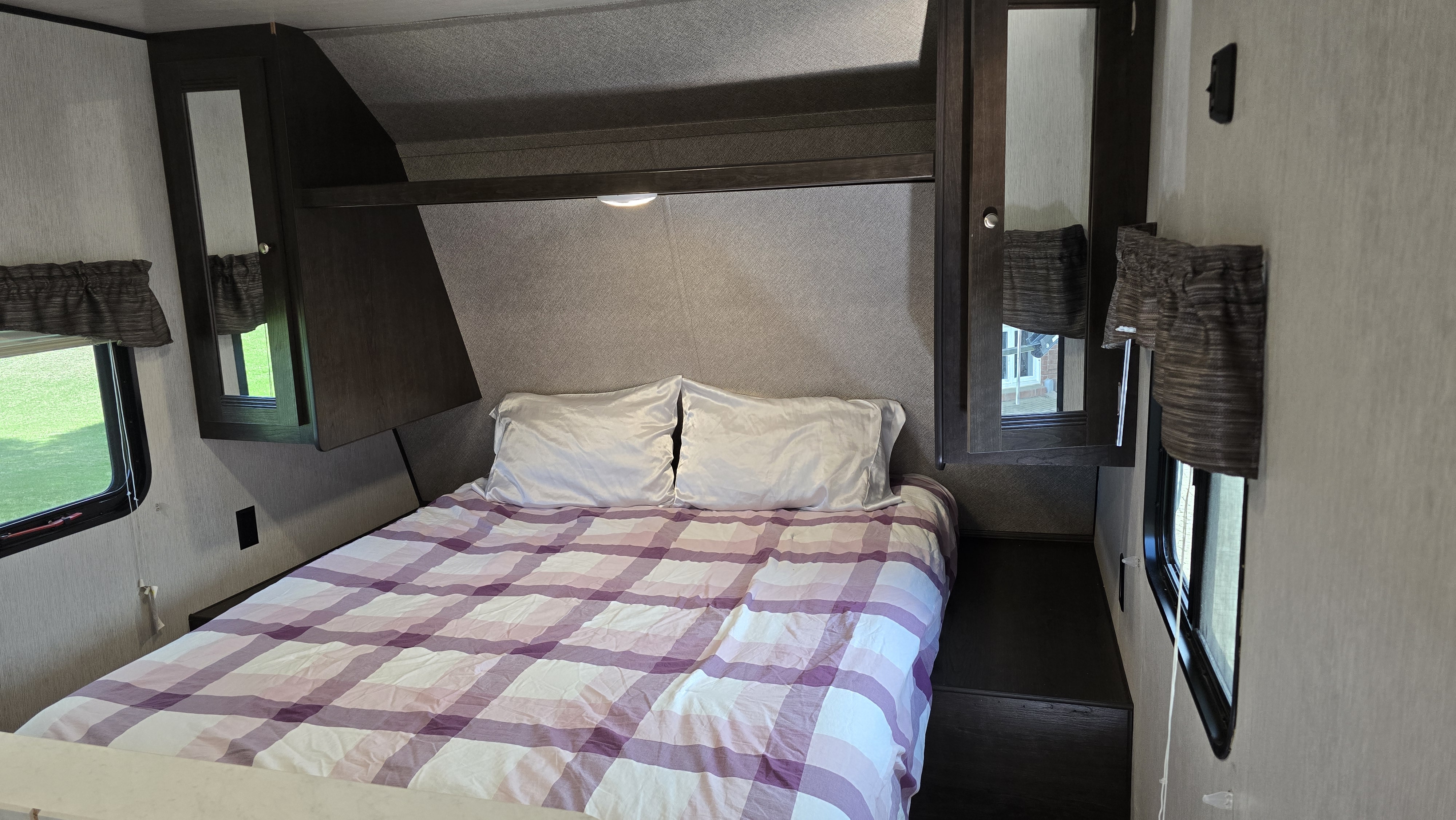 Cozy RV rental bedroom with a plaid bed, mirrored cabinets, and windows offering outdoor views.. Heartland RVs Prowler Lynx 2019